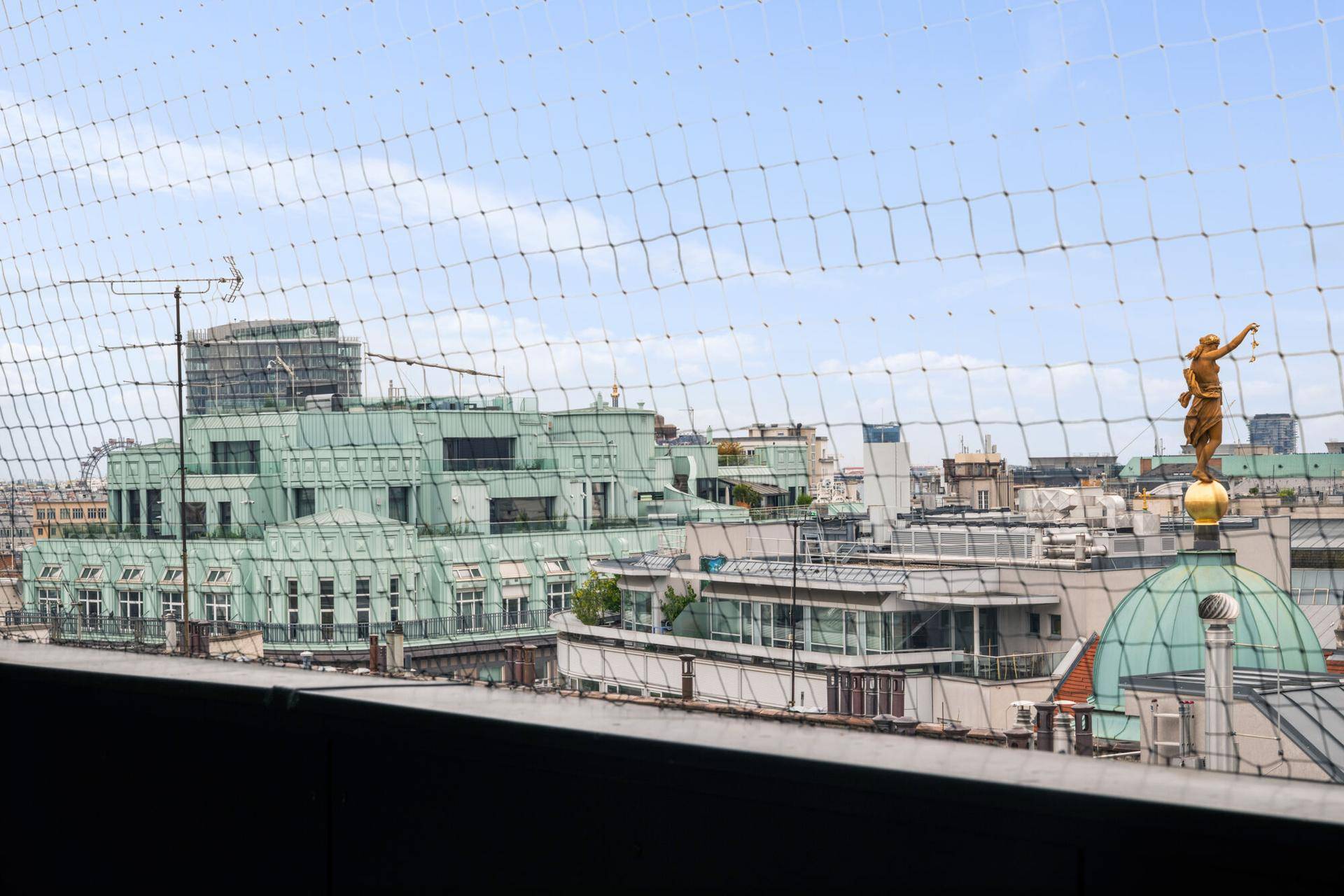 Weitläufiger Stadtblick von der Terrasse mit historischen Dächern und goldener Statue.