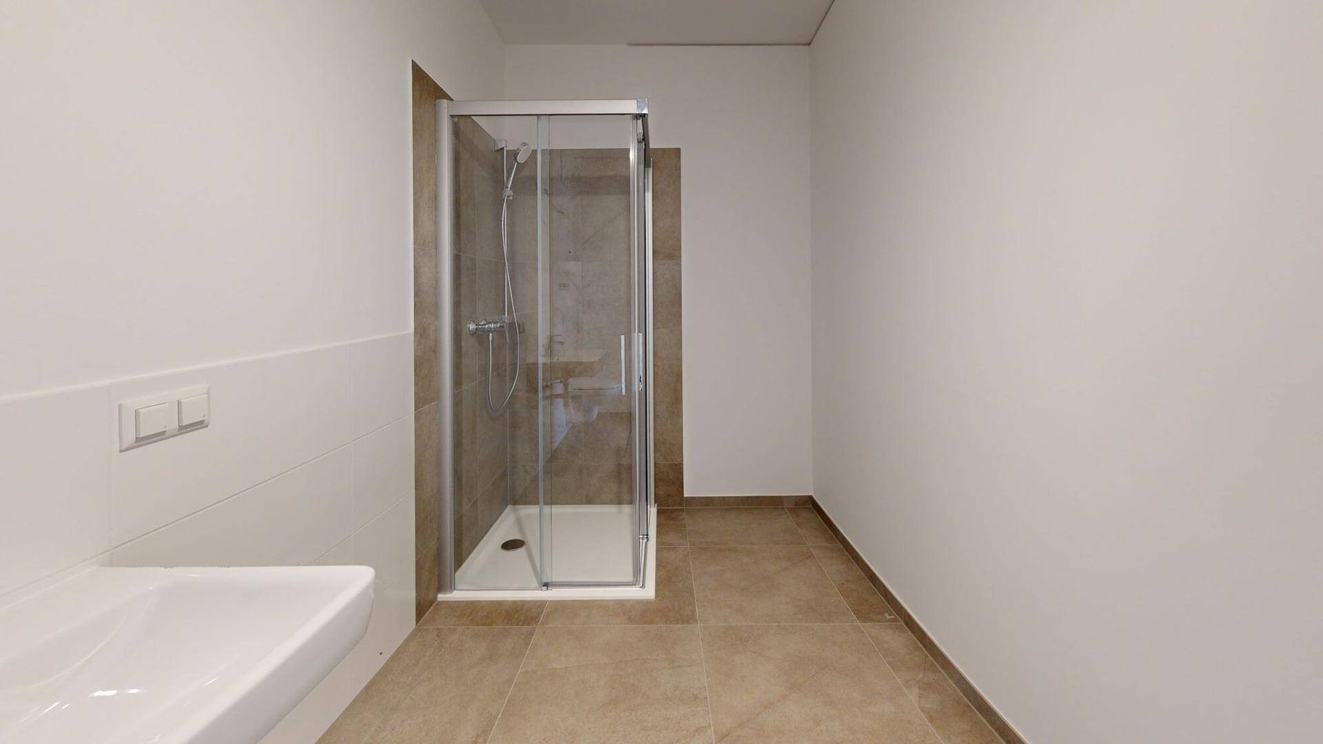 Modernes Badezimmer mit Duschkabine, Waschbecken und hellen Fliesen am Boden.