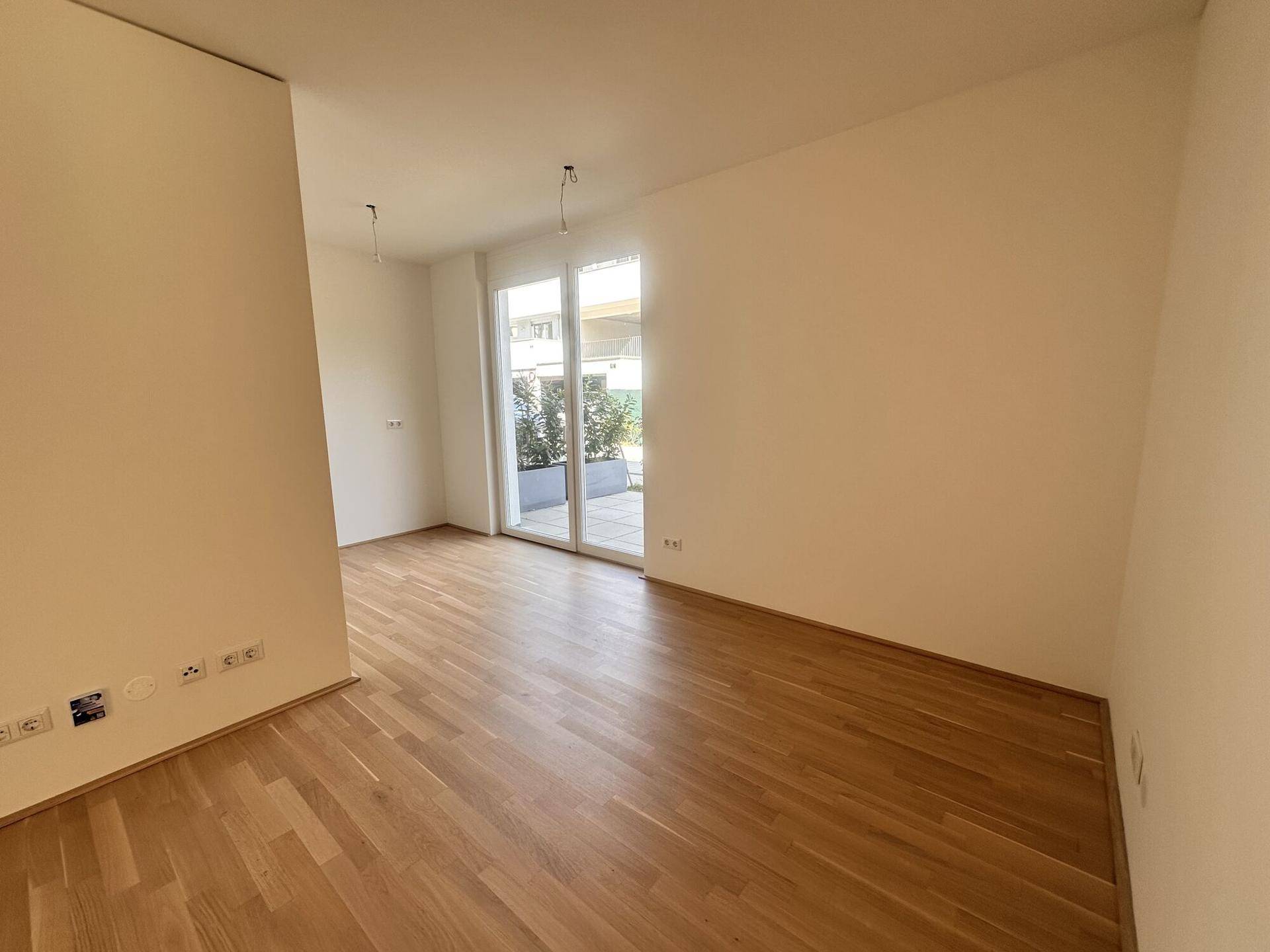 Heller, leerer Raum mit hellem Holzparkettboden und großzügiger Glasschiebetür zum Außenbereich.