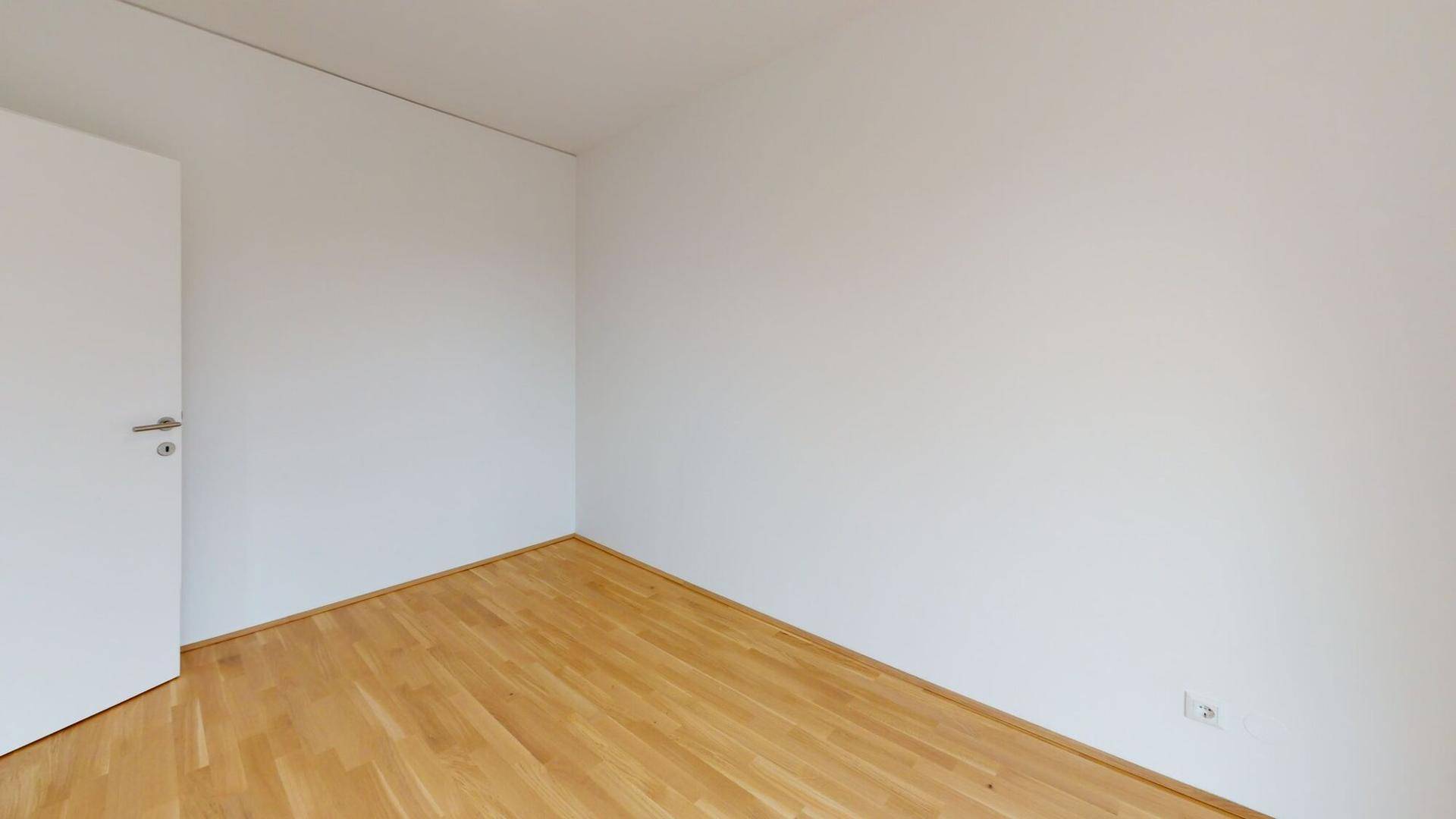 Schlichtes, leeres Zimmer mit hellem Holzboden und weißen Wänden, bereit zur individuellen Gestaltung.