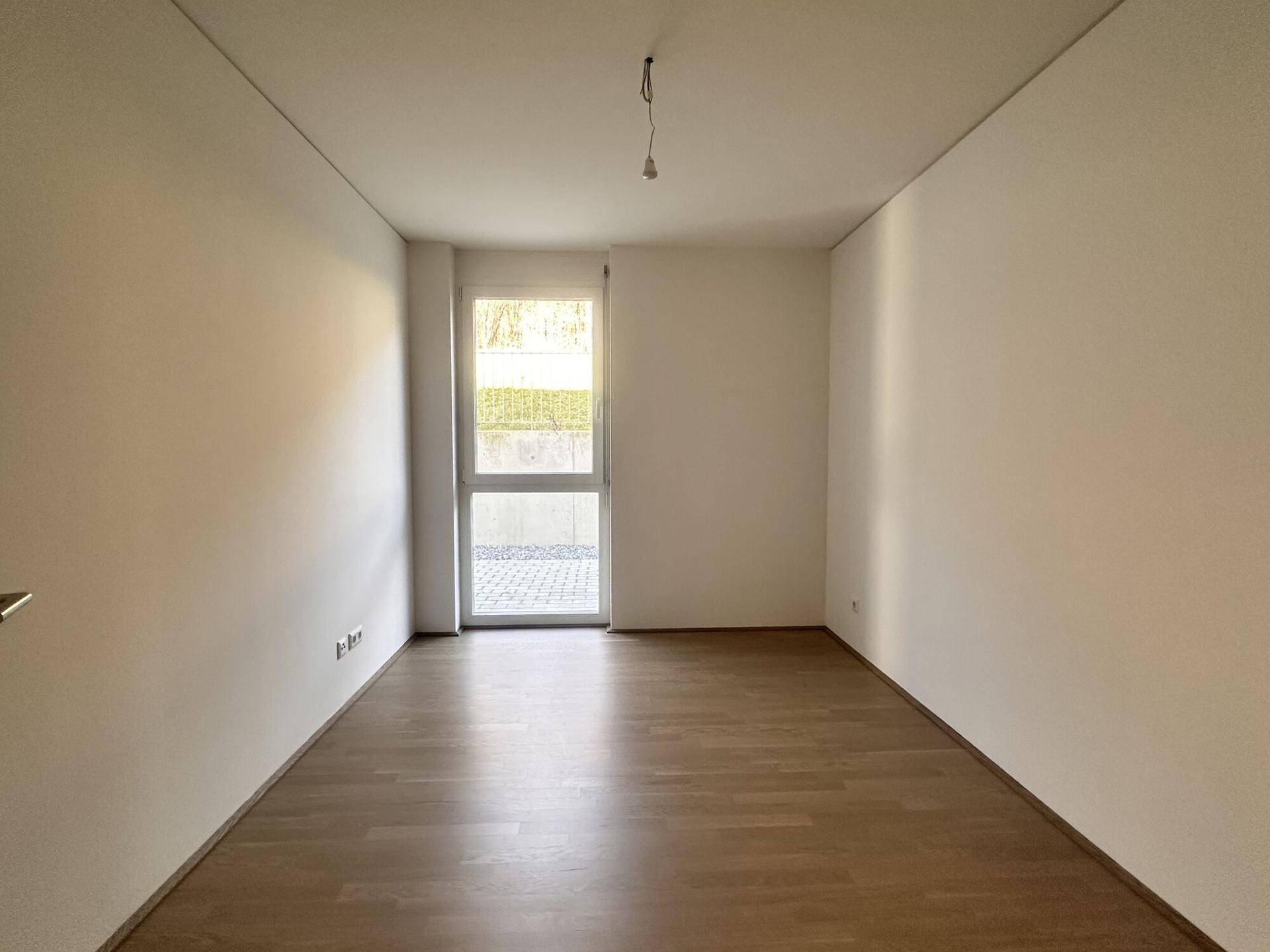 Geräumiges Schlafzimmer mit Parkettboden und großem Fenster mit Zugang zum Außenbereich.