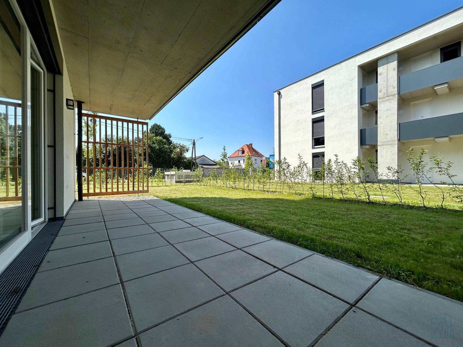 Große gepflasterte Terrasse mit Zugang zum Garten und Blick auf das moderne Gebäude.