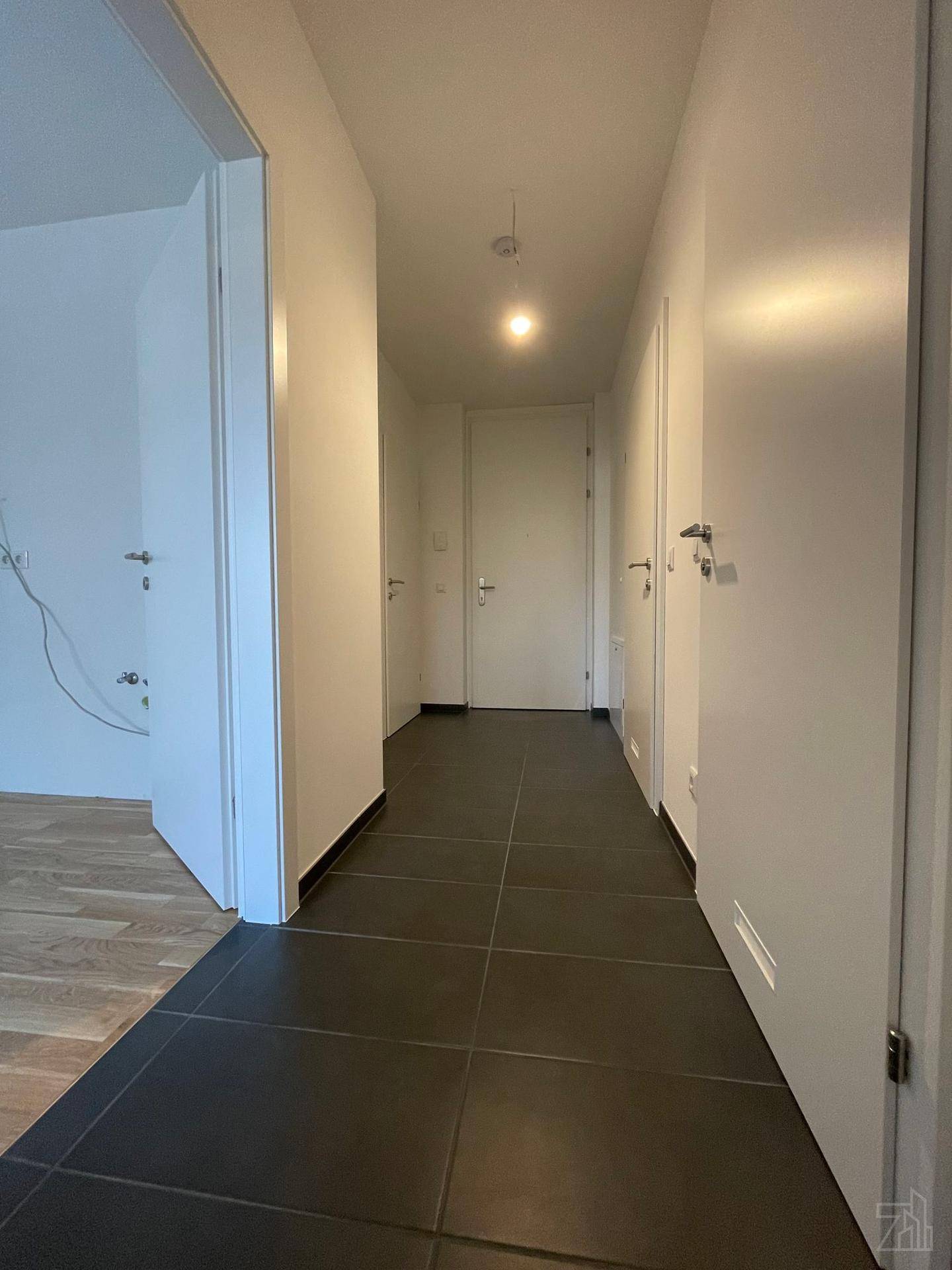 Heller Flur mit dunklen Bodenfliesen und Zugang zu verschiedenen Zimmern der Wohnung.