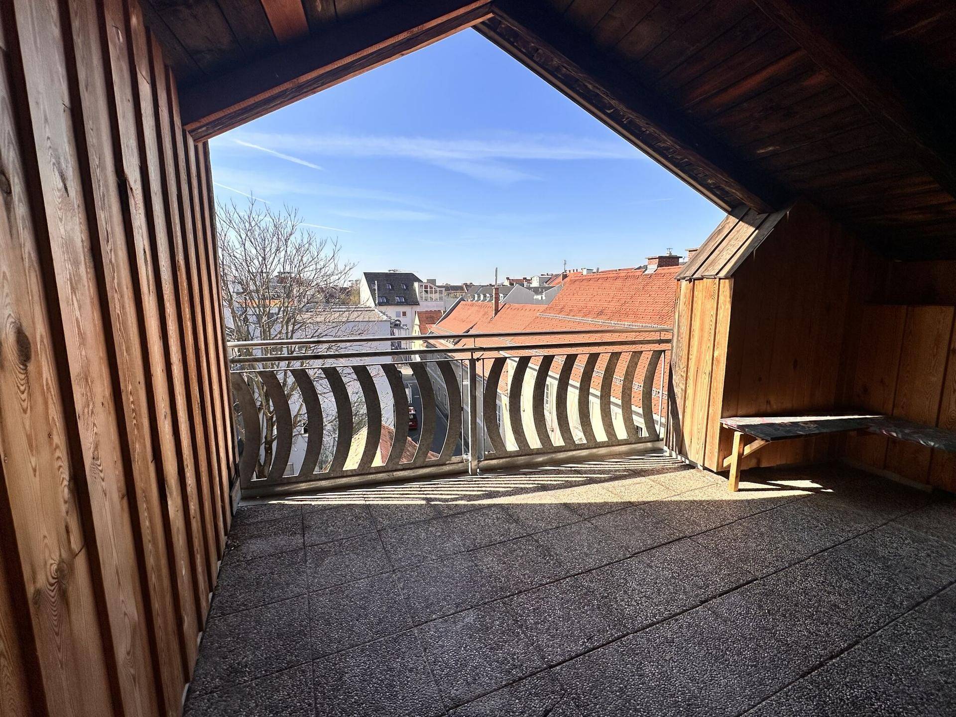 Überdachter Balkon mit Holzwänden und weitem Blick über die Dächer der Stadt.