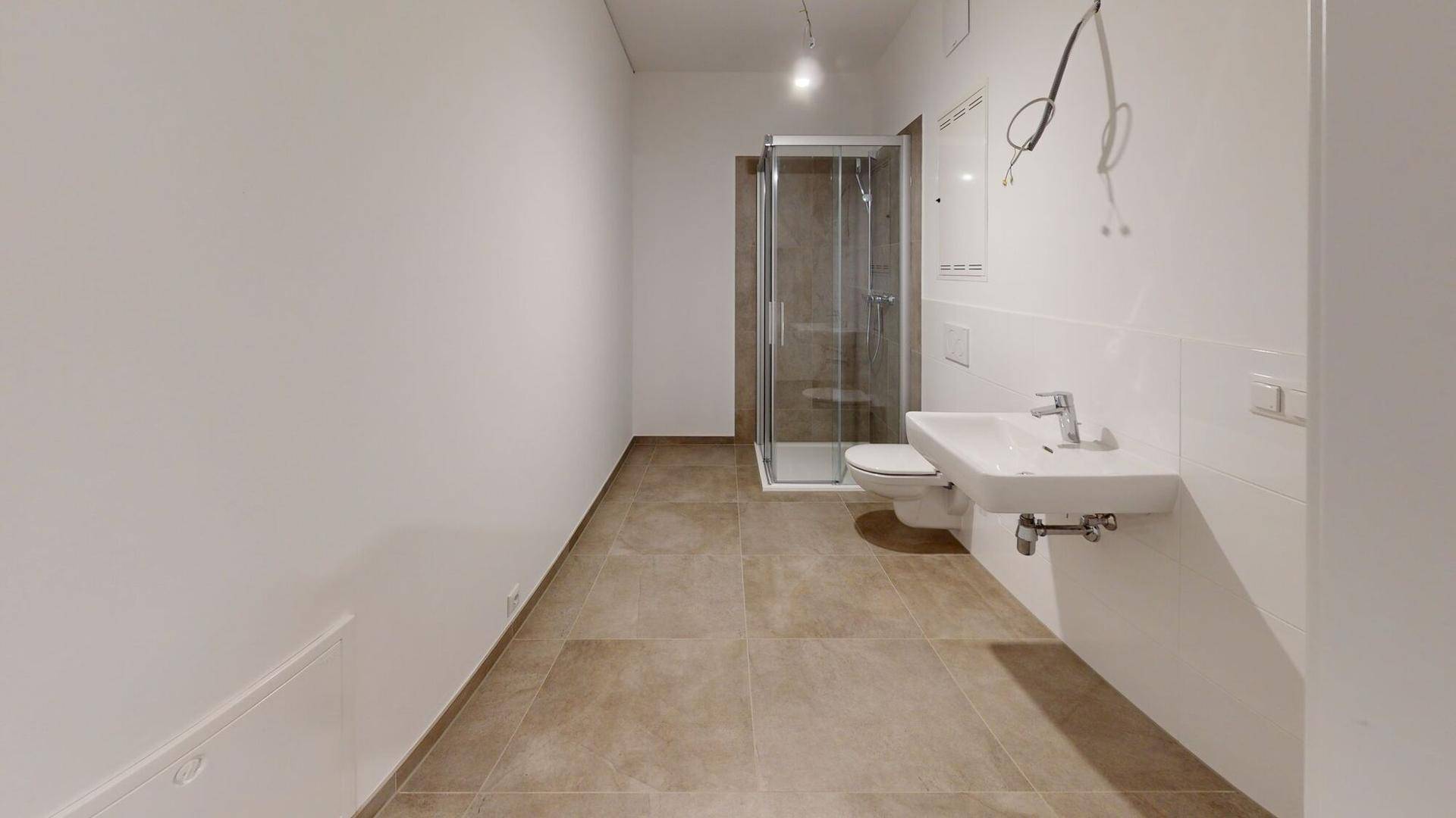 Modernes Badezimmer mit Duschkabine, Wand-WC und Waschbecken auf braunen Fliesen.