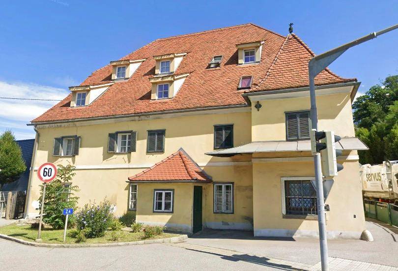 Gelbes Gebäude mit rotem Ziegeldach und Gaubenfenstern an einer Straße.