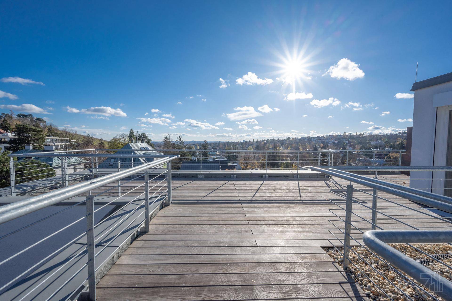 Weitläufige Dachterrasse mit Holzboden, Metallgeländer und Panoramablick unter strahlendem Himmel.