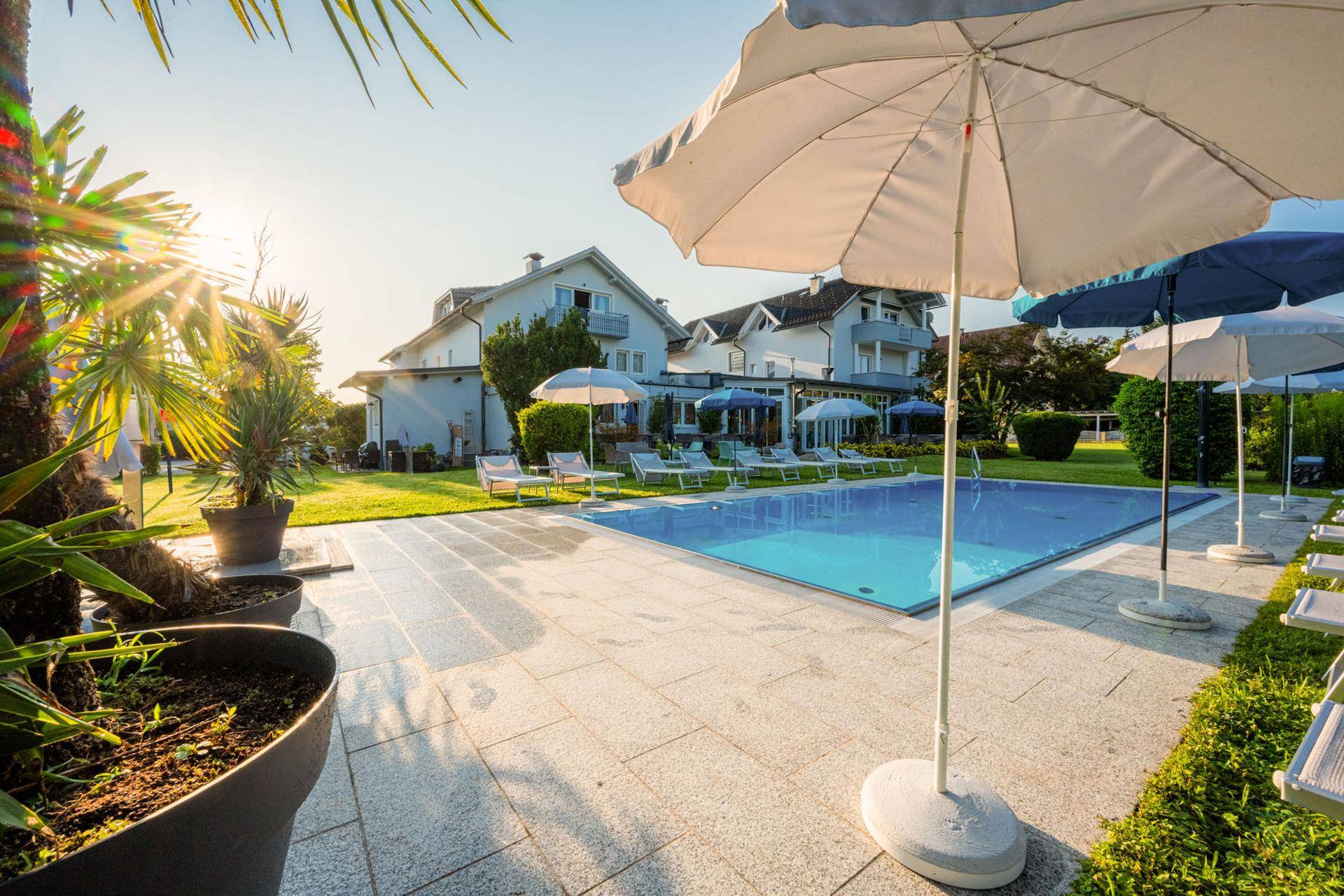 Großer Außenpoolbereich mit Liegestühlen, Sonnenschirmen und Palmen in sonniger Lage.