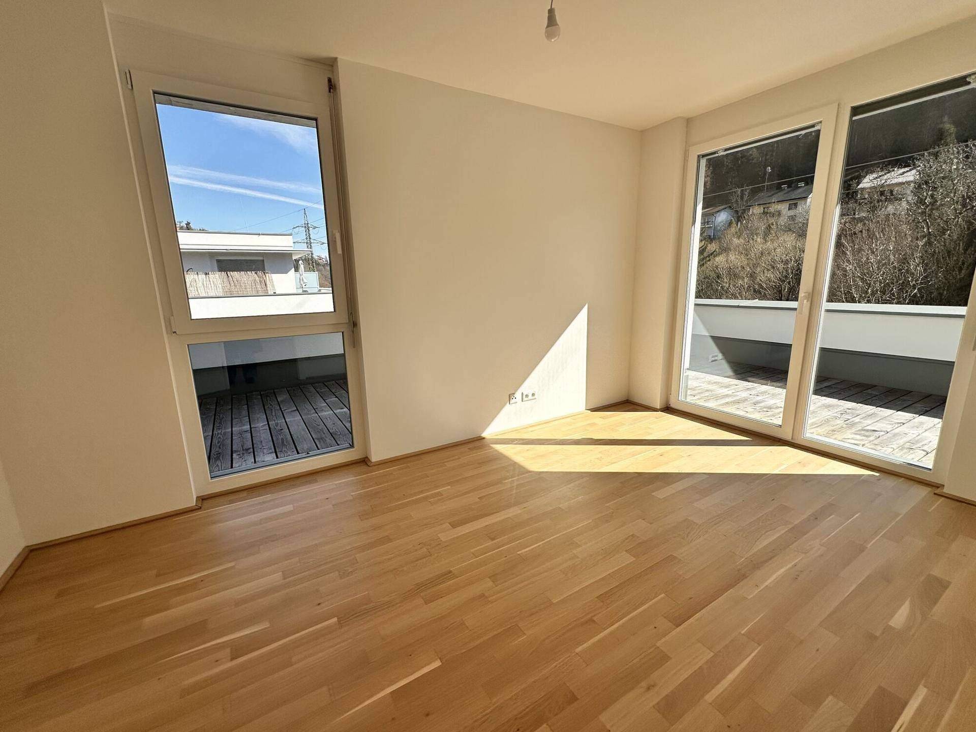 Lichtdurchflutetes Zimmer mit Parkettboden und großen Terrassentüren, die viel Sonnenlicht hereinlassen.