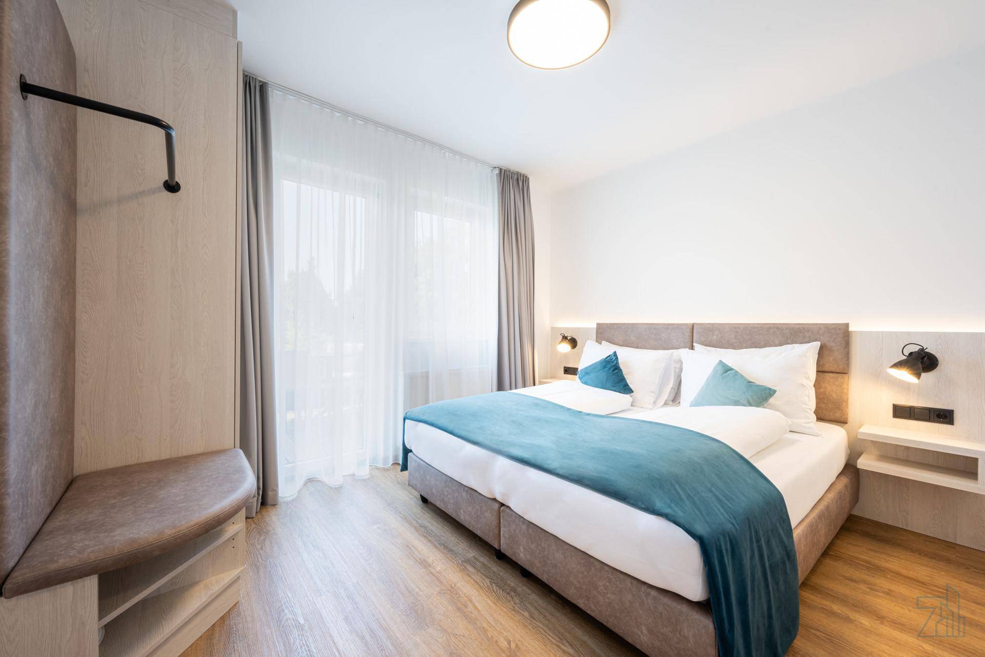 Gemütliches Schlafzimmer mit Doppelbett, Holzboden und großem Fenster für viel Tageslicht.
