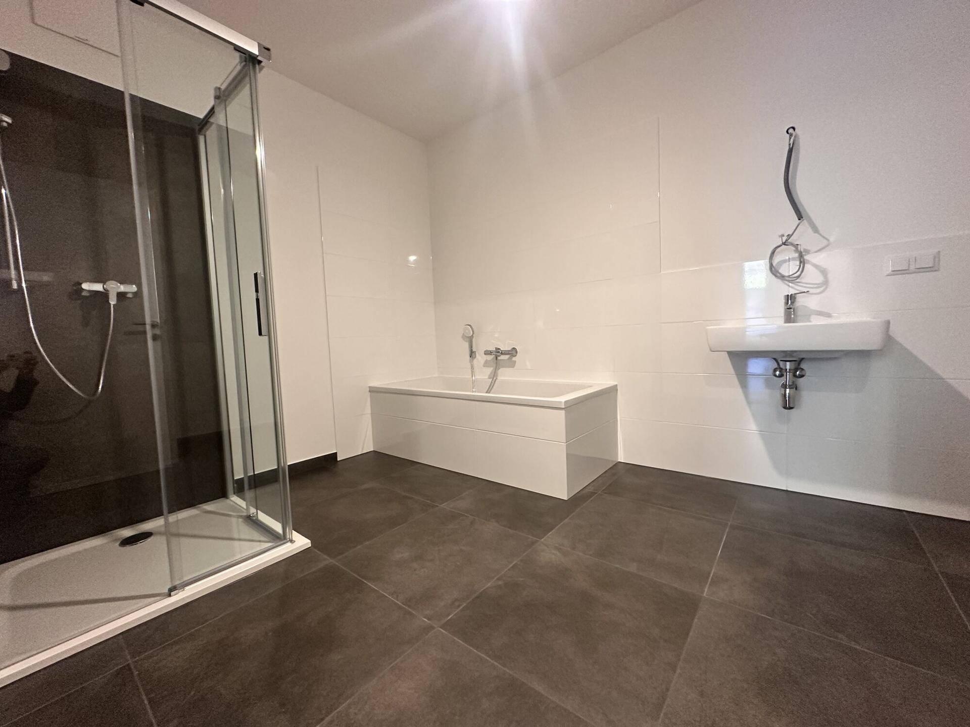 Modernes Badezimmer mit Badewanne, Duschkabine und dunklen Bodenfliesen.