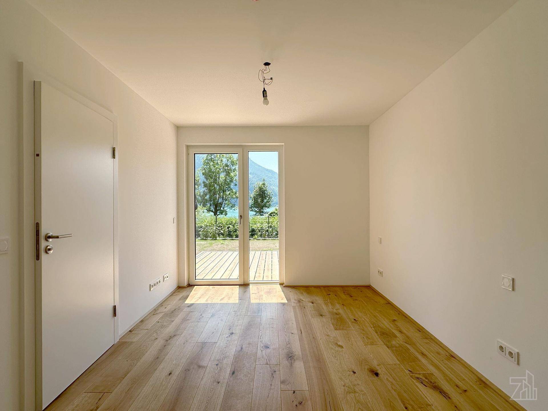 Geräumiges Schlafzimmer mit Holzboden und Glastür, die einen direkten Blick auf den See bietet.