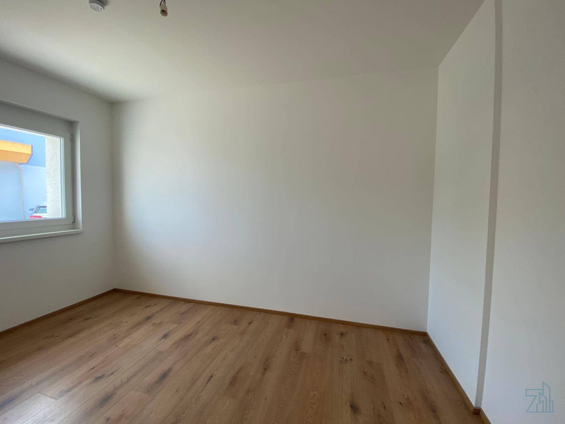Leeres Schlafzimmer mit hellem Holzfußboden und einem Fenster für Tageslicht.