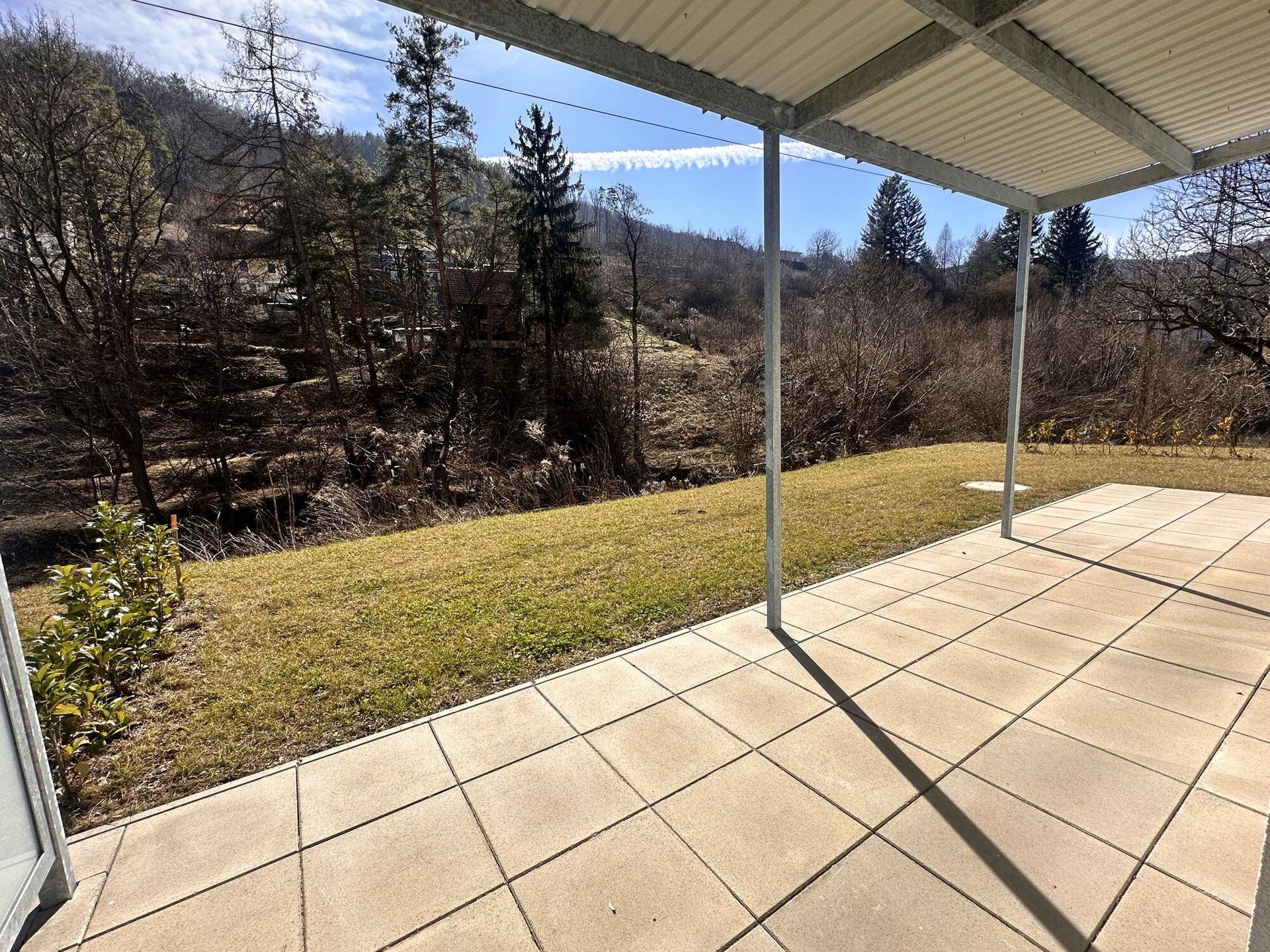 Überdachte Terrasse mit Fliesenboden und Blick auf die umliegende Natur.