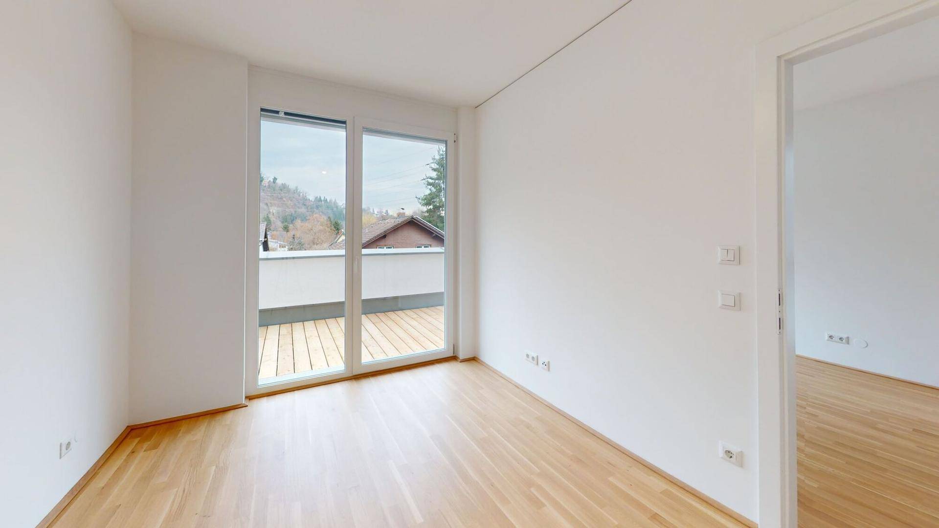 Helles Schlafzimmer mit Holzboden und großer Glastür, die zu einer Holzterrasse führt.