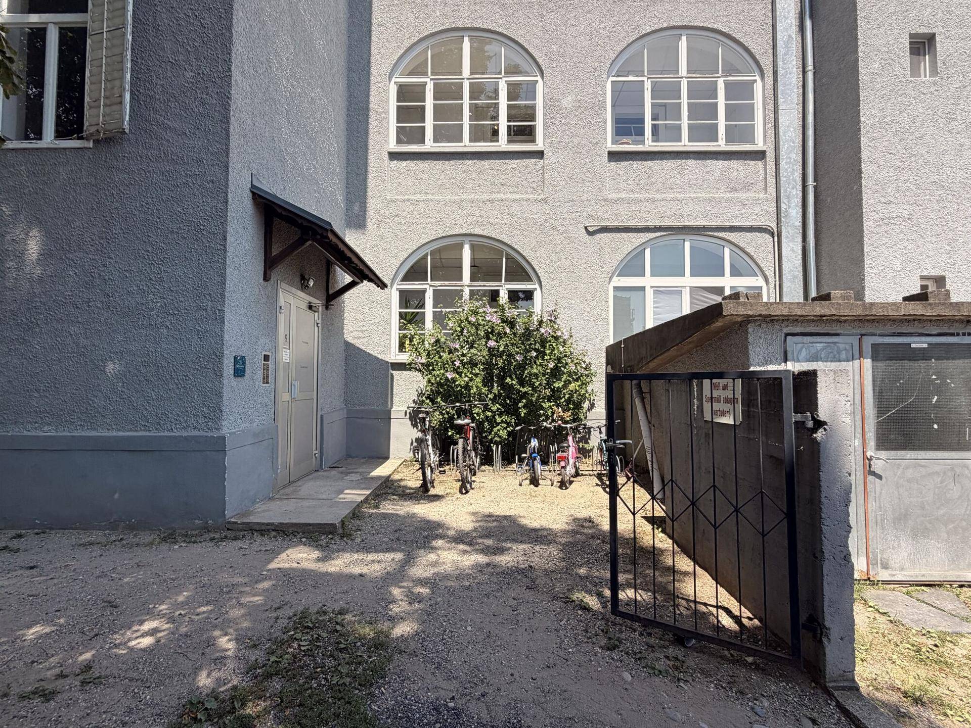 Eingangsbereich des Gebäudes mit Fahrradabstellplatz und einem kleinen Tor.