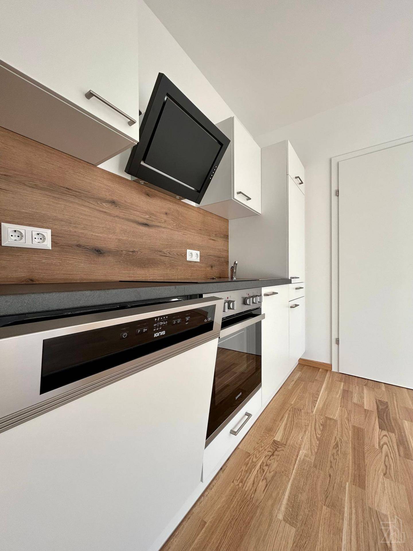 Moderne Einbauküche mit weißen Schränken, Holzakzenten und integrierten Geräten.
