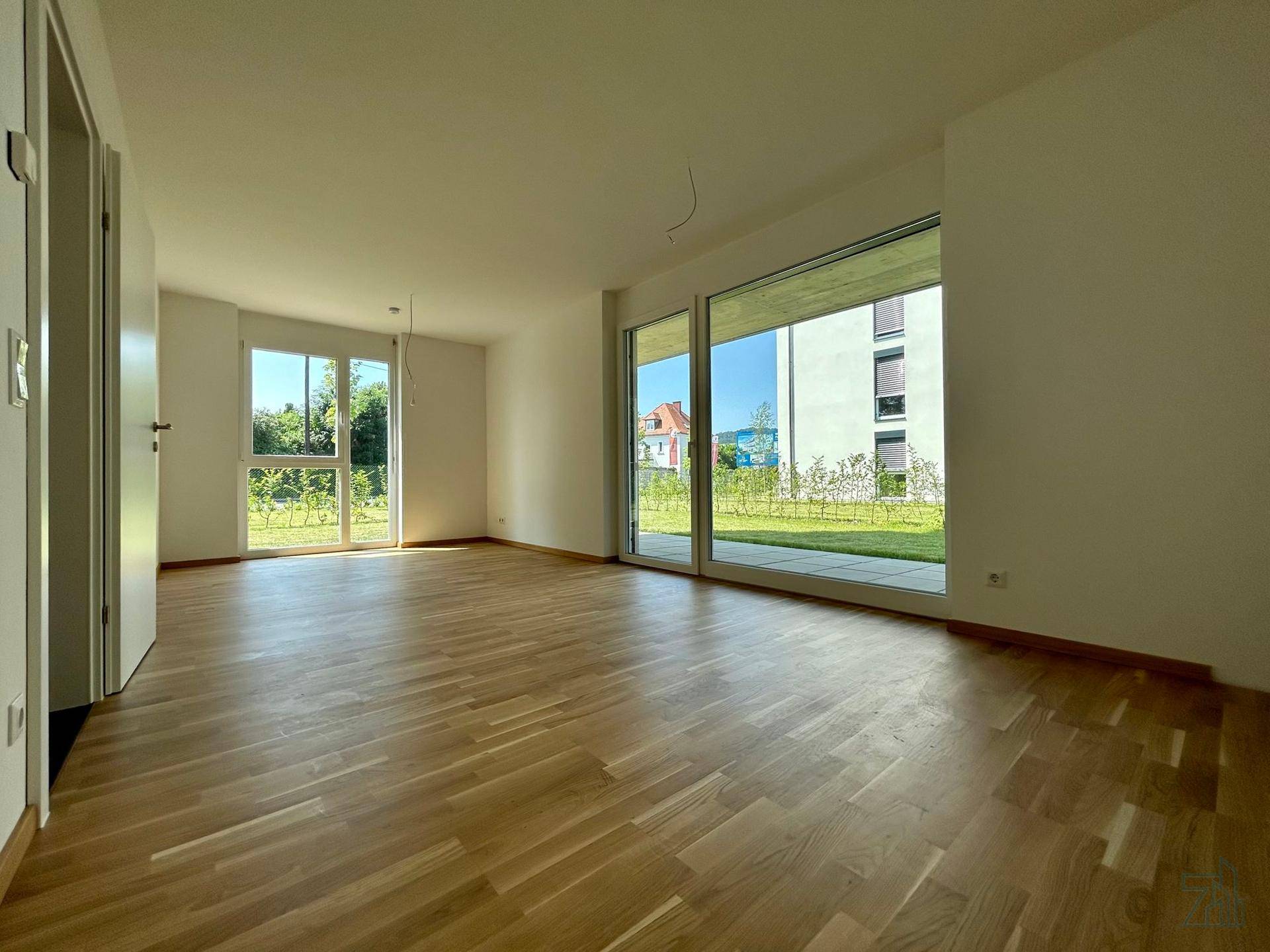 Geräumiger Wohnbereich mit hellem Parkettboden und großen Fenstern mit Blick ins Grüne.