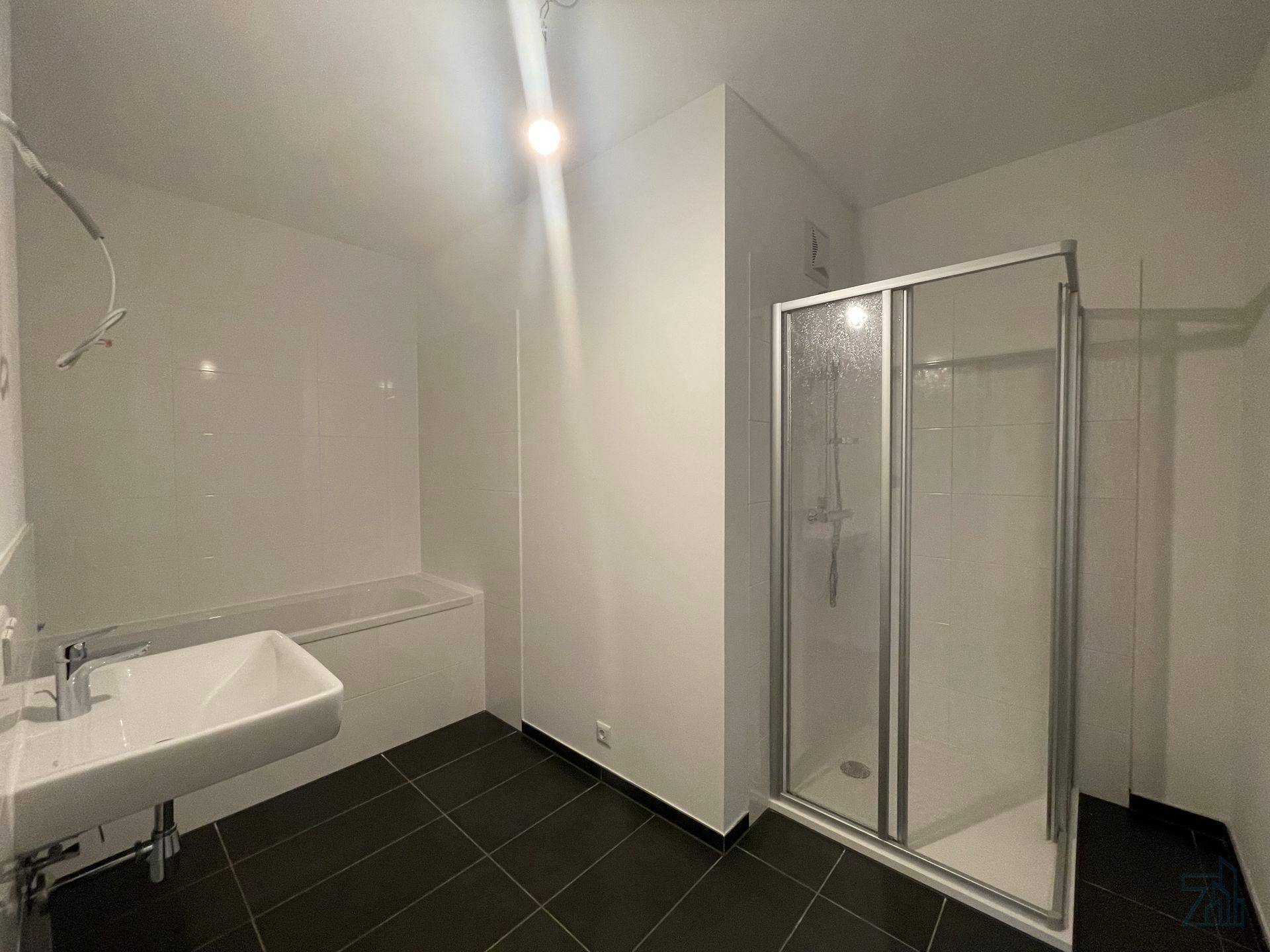 Badezimmer mit dunklen Fliesen, Badewanne, Waschbecken und einer Duschkabine.