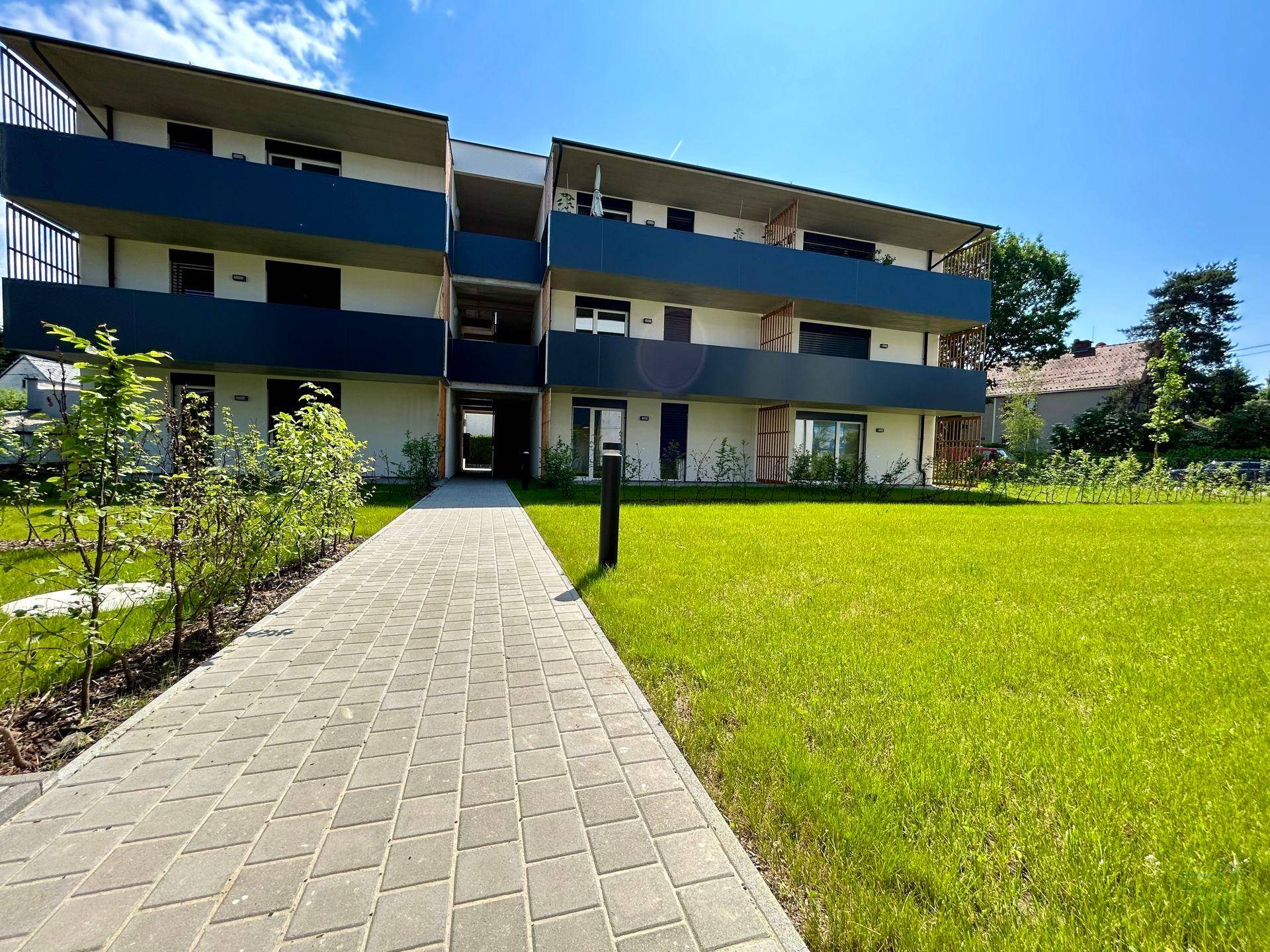 Modernes Mehrfamilienhaus mit gepflastertem Weg und weitläufiger Grünfläche im Freien.