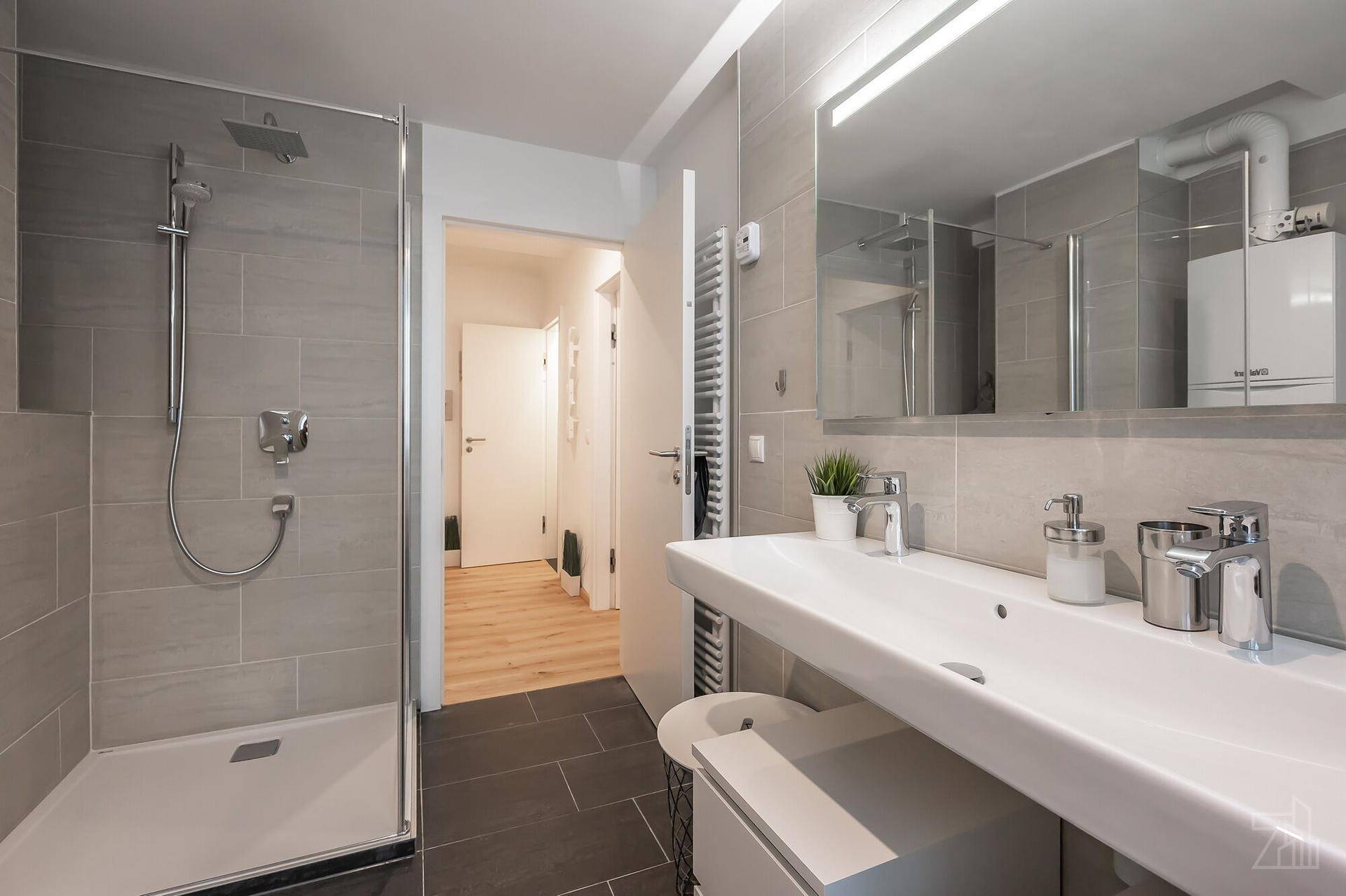 Modernes Badezimmer mit begehbarer Dusche, Einzelwaschbecken und grauen Fliesen.
