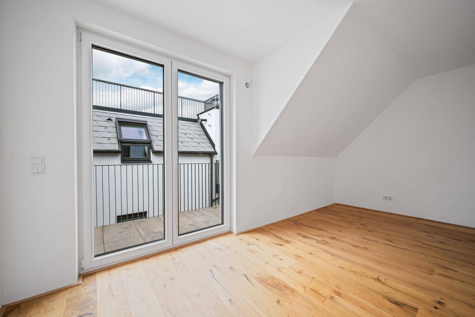 Helles Dachgeschosszimmer mit Holzboden und Balkontür, bietet Zugang ins Freie.