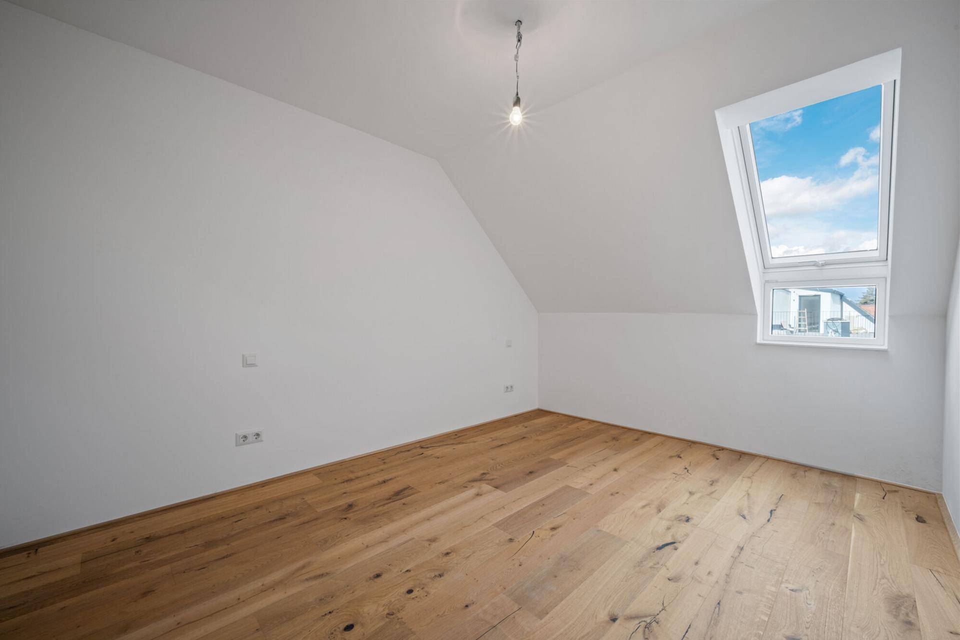 Leeres Zimmer im Dachgeschoss mit Holzboden und einem großen Dachfenster, das viel Licht hereinlässt.