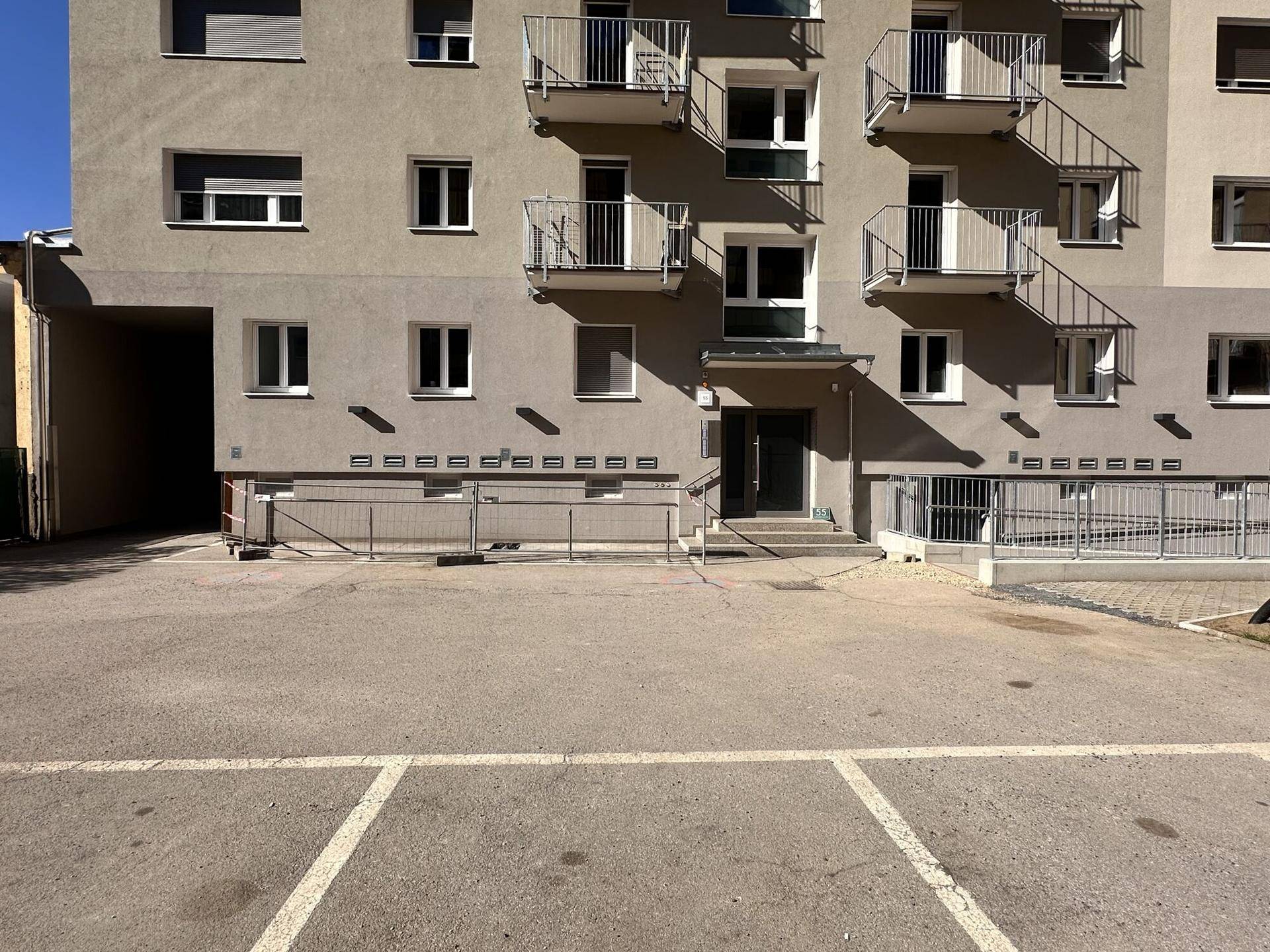 Eingangsbereich eines Mehrfamilienhauses mit Balkonen, Parkplätzen und einer Rollstuhlrampe.