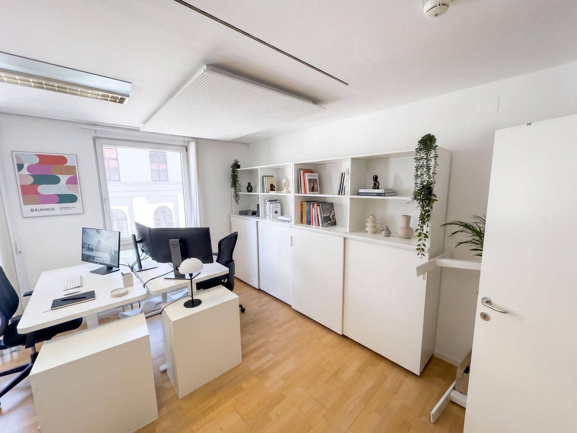 Geräumiges und helles Büro mit funktionalen Arbeitsplätzen, weißen Schränken und Regalen für Stauraum.