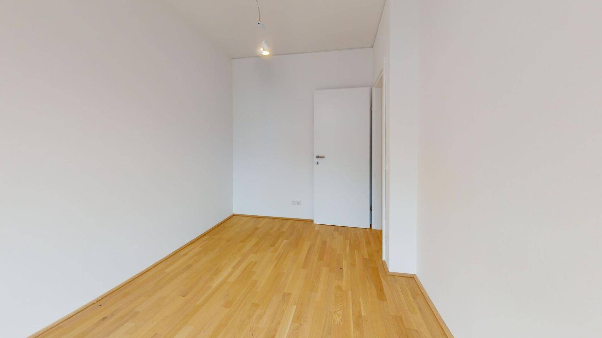 Heller, leerer Raum mit Holzboden und weiß gestrichenen Wänden, ideal als Schlafzimmer.