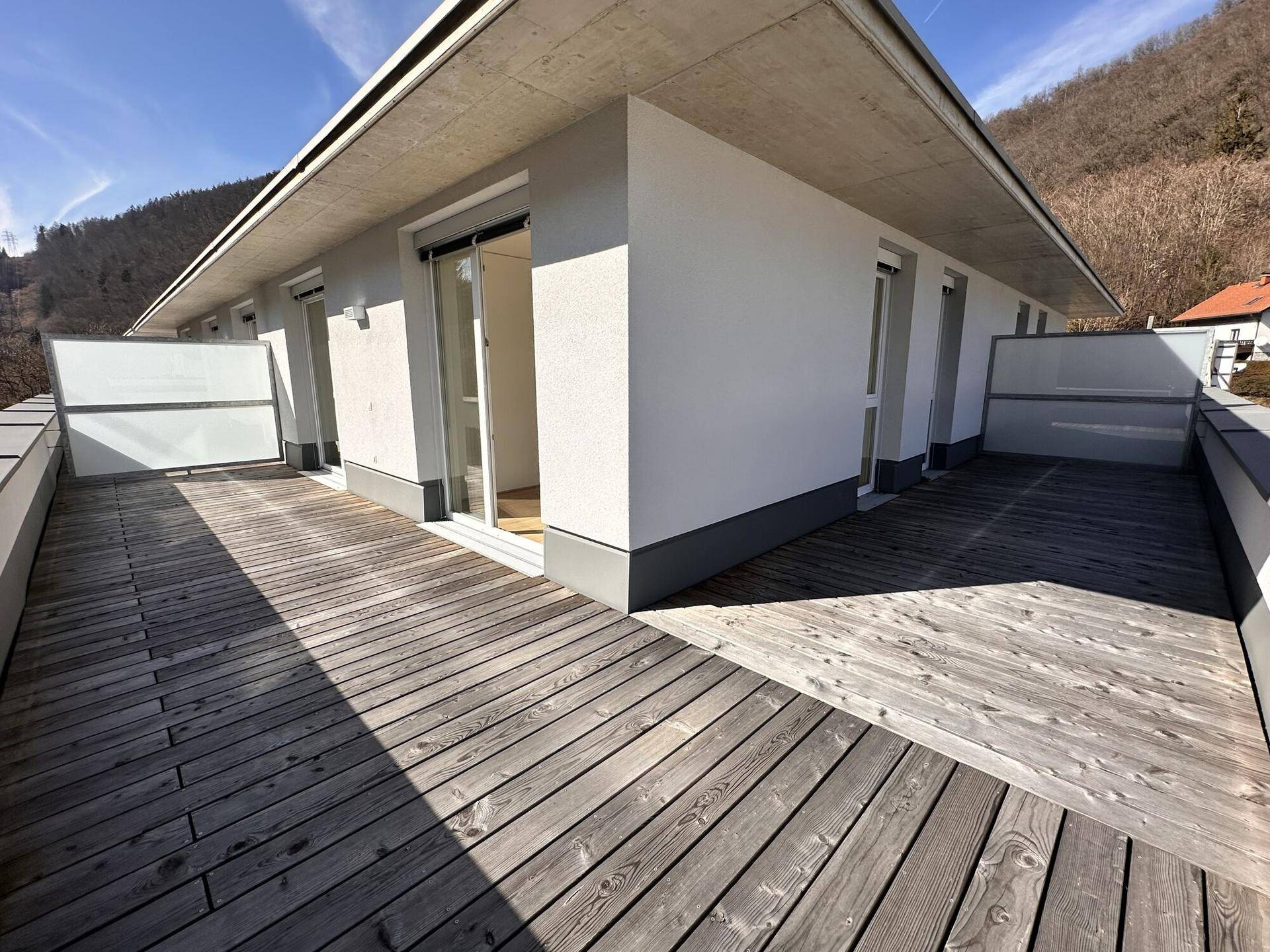 Weitläufige Dachterrasse mit Holzboden und Blick auf die moderne Architektur des Gebäudes und die Umgebung.