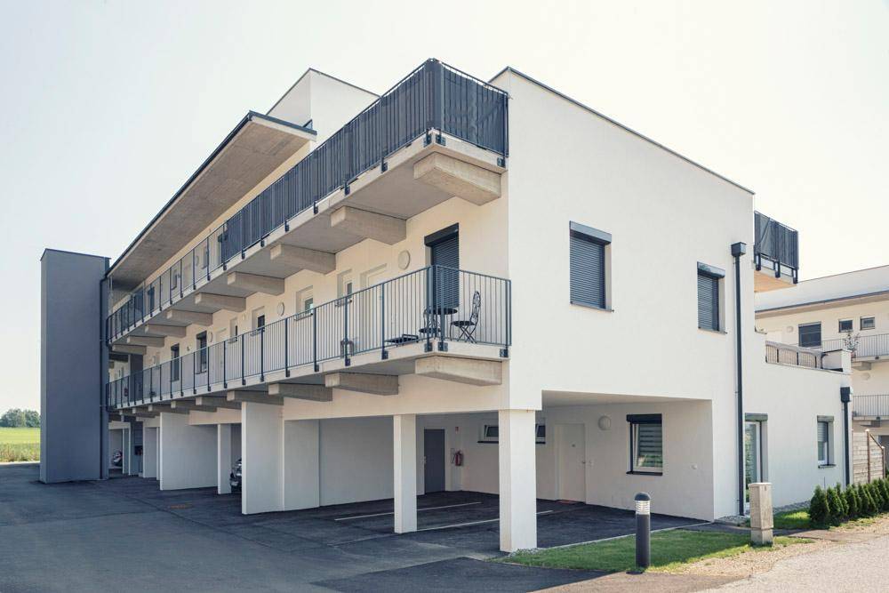 Neubau-Wohngebäude mit moderner Architektur, Balkonen und überdachten Parkplätzen im Erdgeschoss.