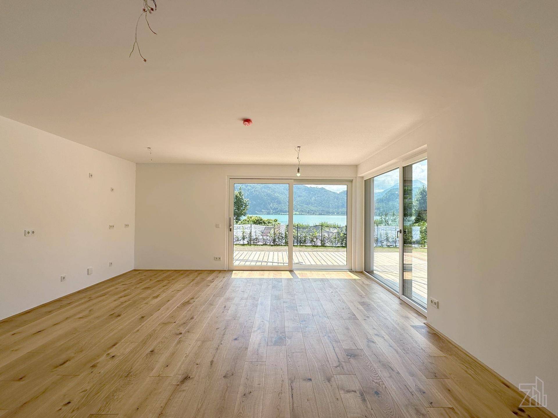 Lichtdurchfluteter Wohnbereich mit hellem Holzboden und großen Fensterfronten, die einen herrlichen Seeblick ermöglichen.