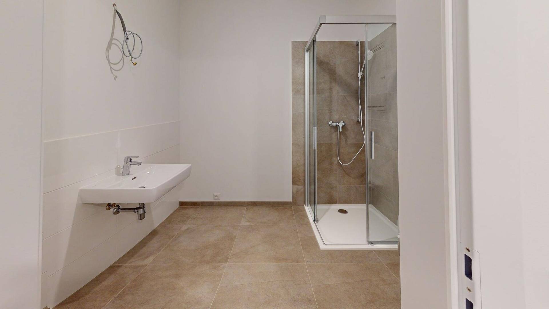 Modernes Badezimmer mit Duschkabine, Wandwaschbecken und hellbraunen Fliesen.