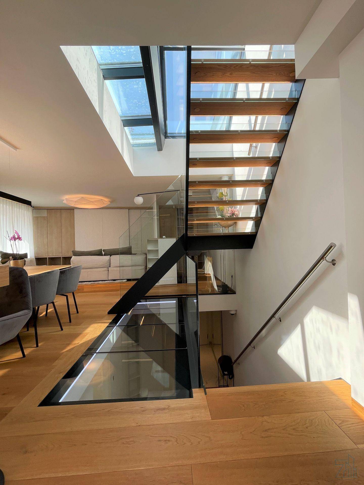 Moderne Treppe mit Glasgeländer und Holzstufen, die zu einem unteren Bereich führt, mit Oberlicht.