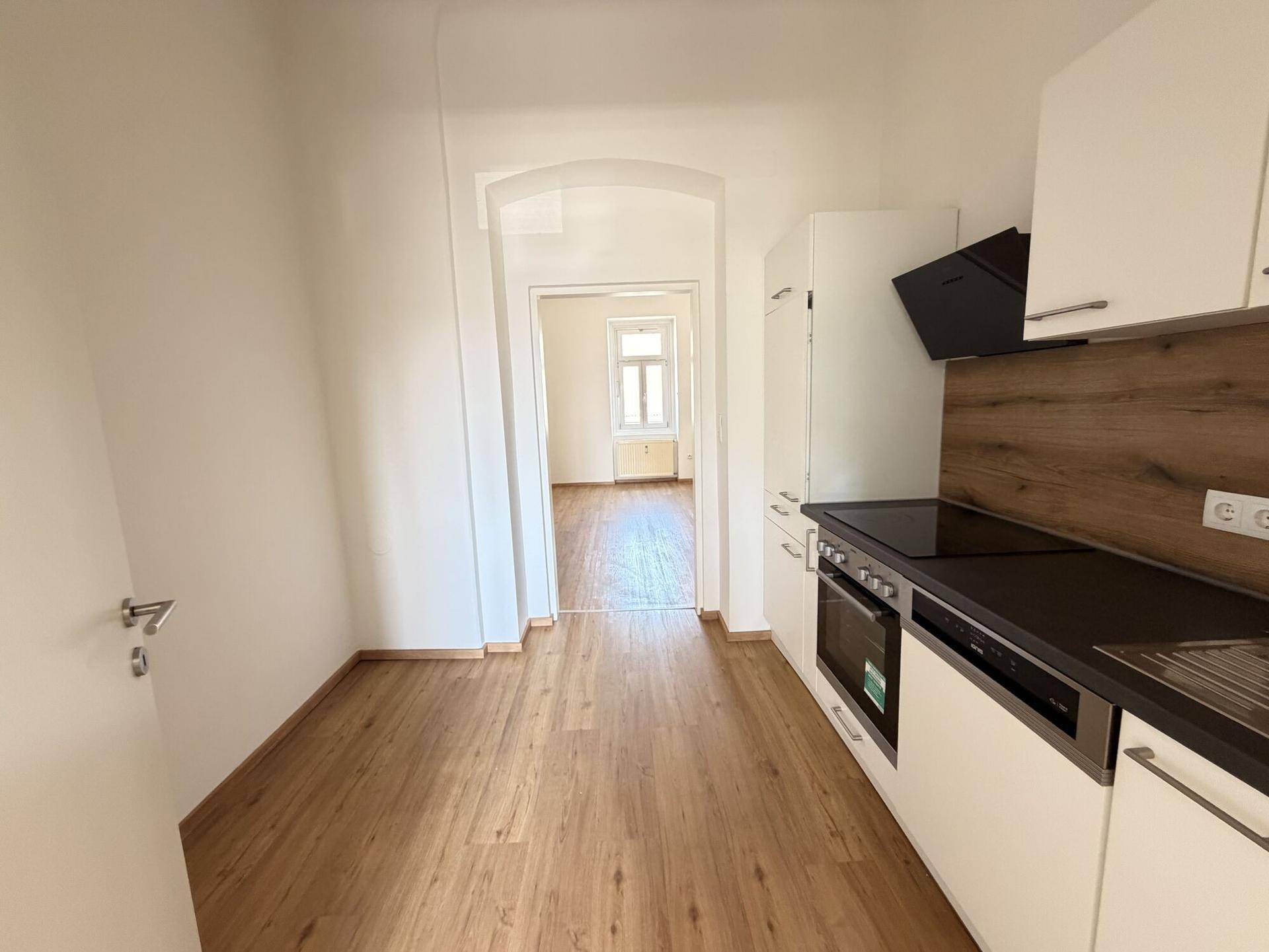 Offene Küche mit Laminatboden und Blick durch einen Bogen in einen weiteren Raum.