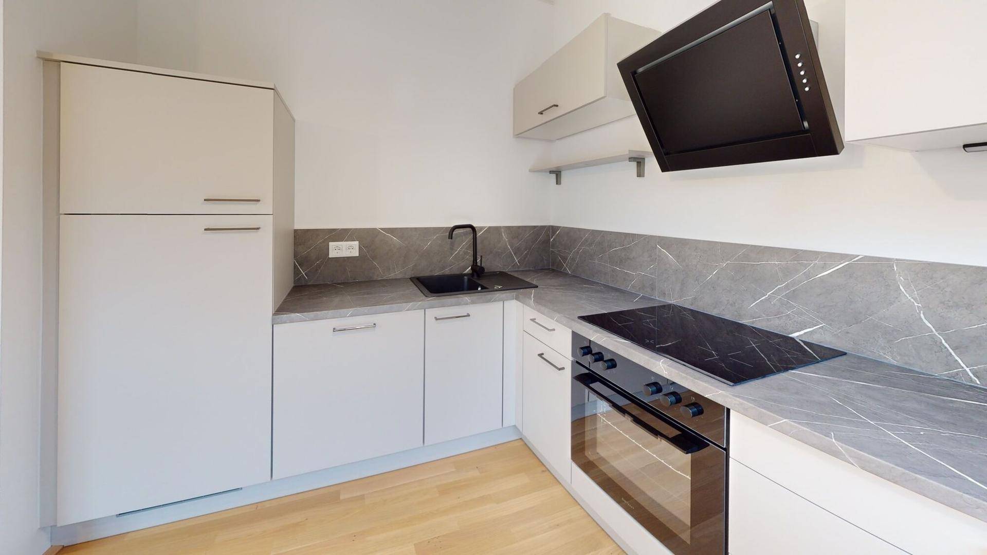 Detailansicht der modernen Küche mit Induktionskochfeld, Backofen und dunkler Arbeitsplatte.