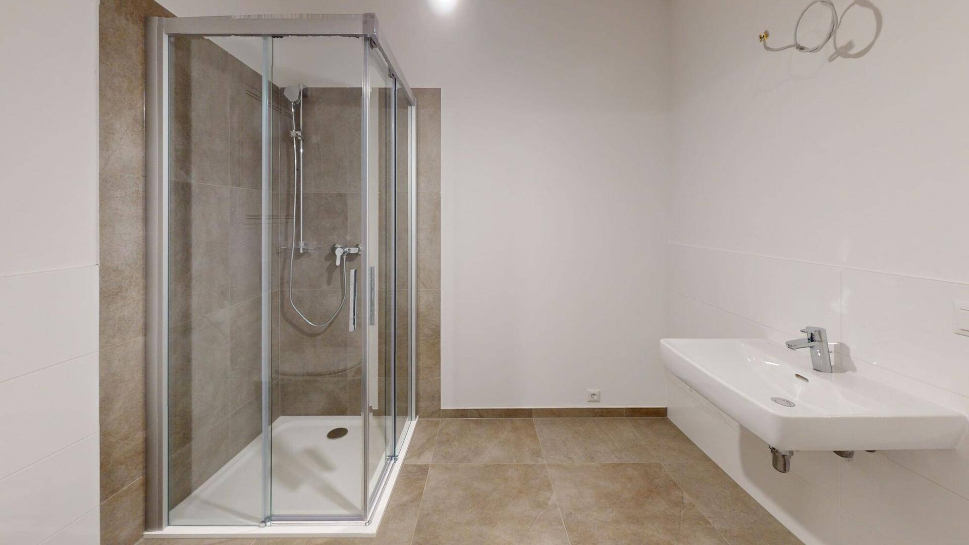 Modernes Badezimmer mit großer Duschkabine, weißem Waschbecken und hellbraunen Fliesen.