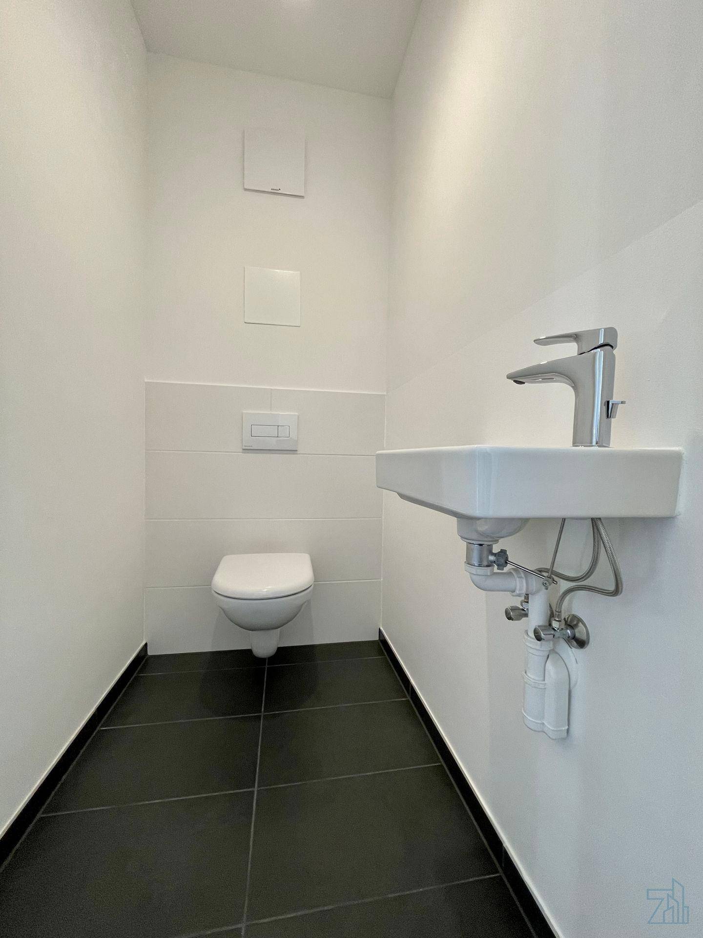 Separates Gäste-WC mit wandhängendem WC, Waschbecken und dunklen Bodenfliesen.