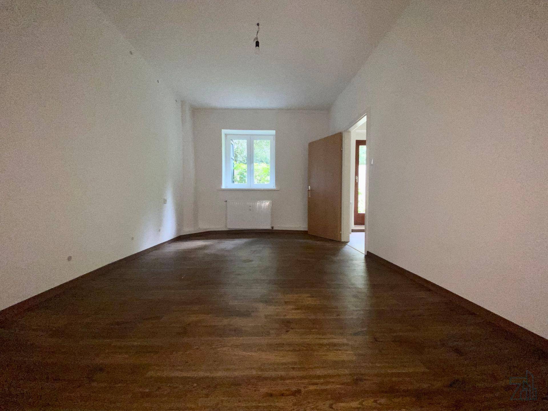 Geräumiges Zimmer mit Holzboden und Fenster, das vielseitig nutzbar ist.