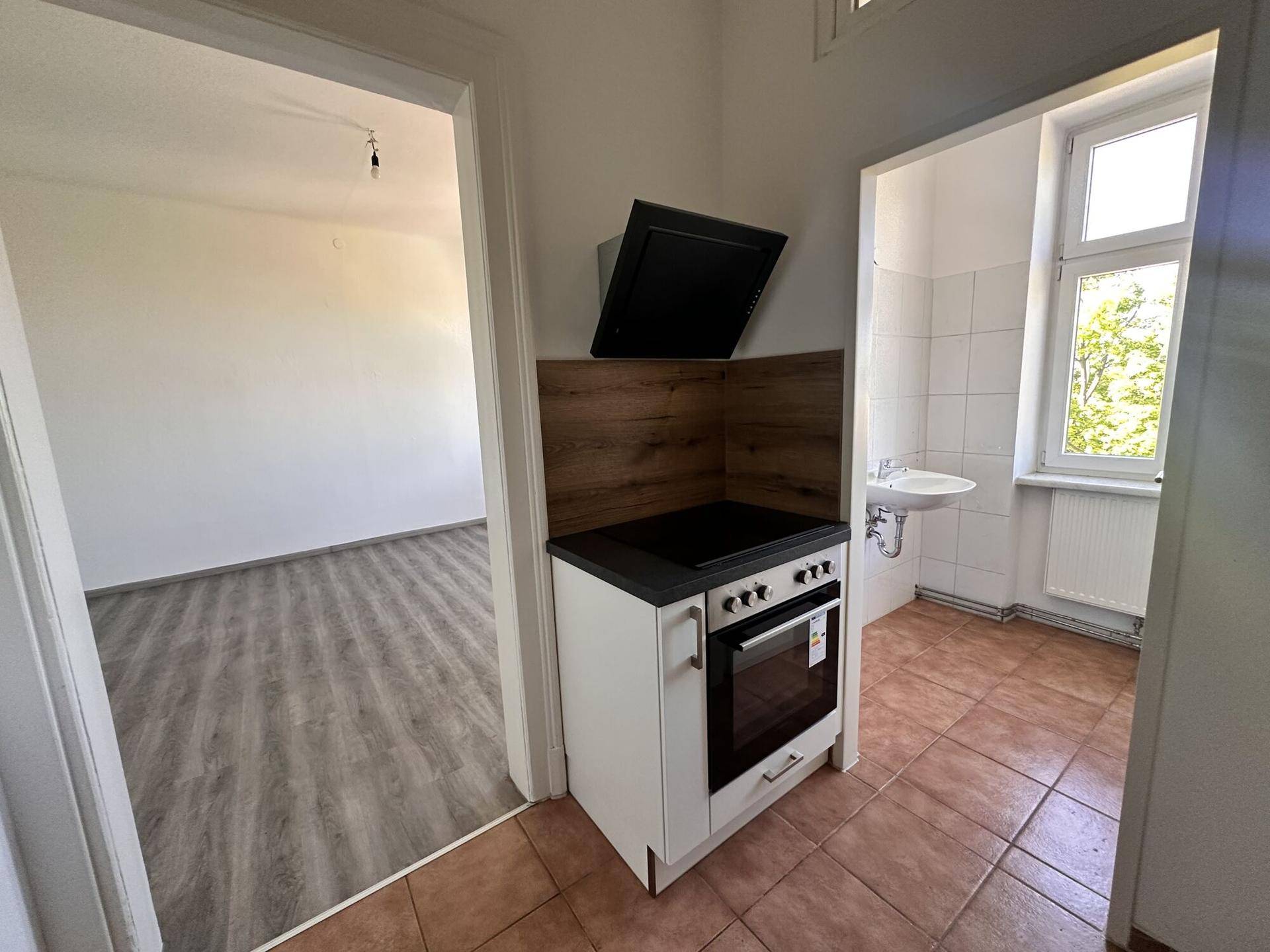 Blick von einem Zimmer in eine Küche mit Herd, Dunstabzugshaube und Terrakotta-Fliesenboden.