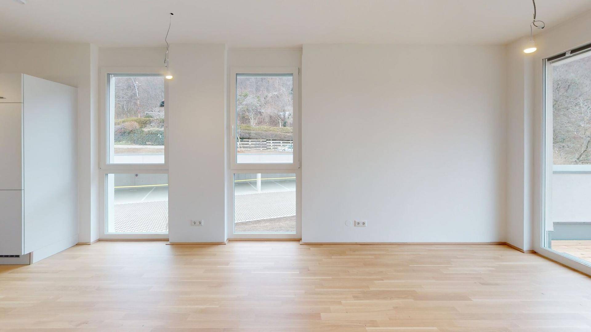 Heller Raum mit Holzboden und großen Fenstern, ideal für einen offenen Wohnbereich.