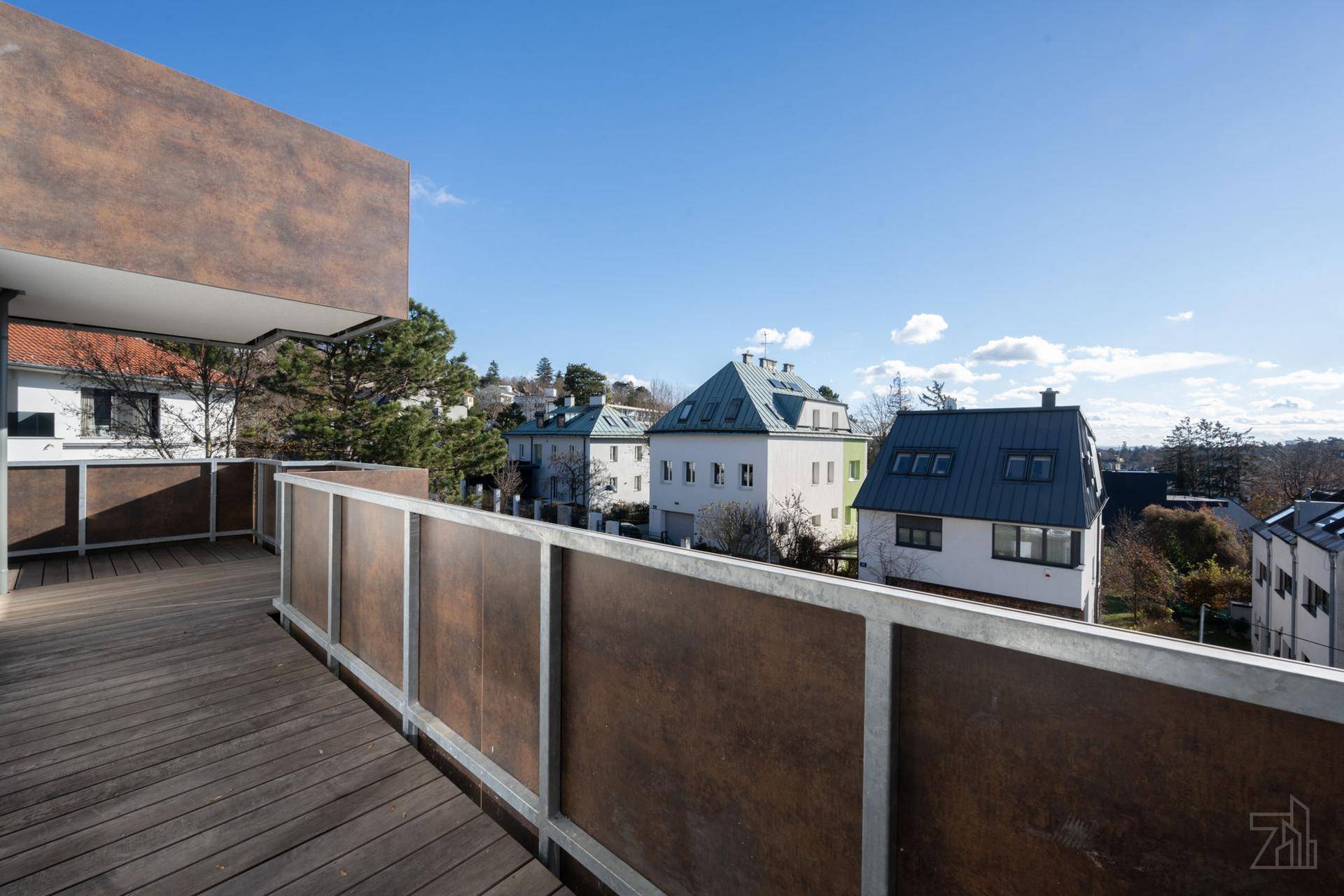 Großer Balkon mit Holzboden und Blick auf die umliegenden Häuser und grüne Landschaft.