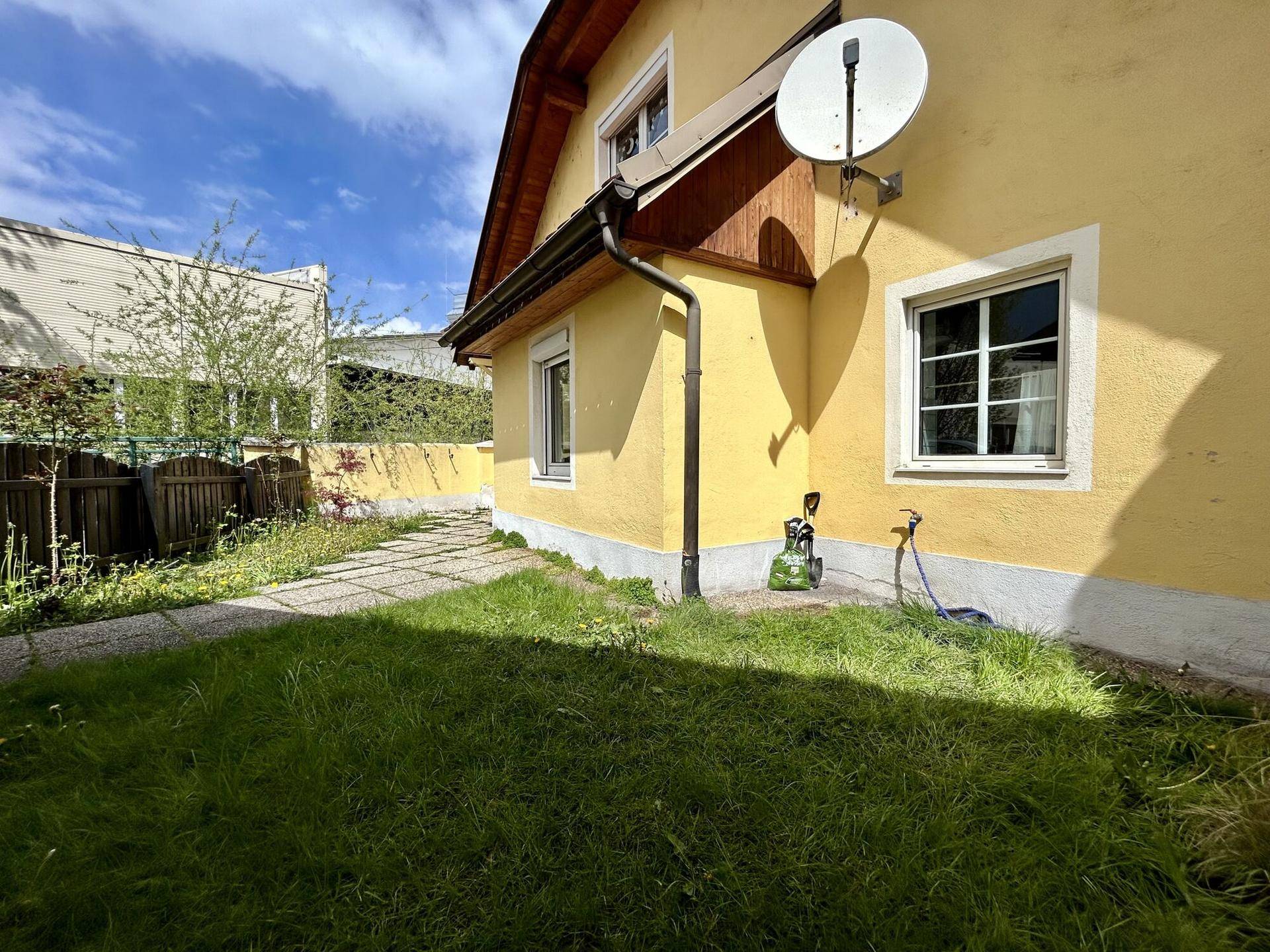 Kleiner Gartenbereich neben dem Haus mit Rasenfläche und gepflastertem Weg.