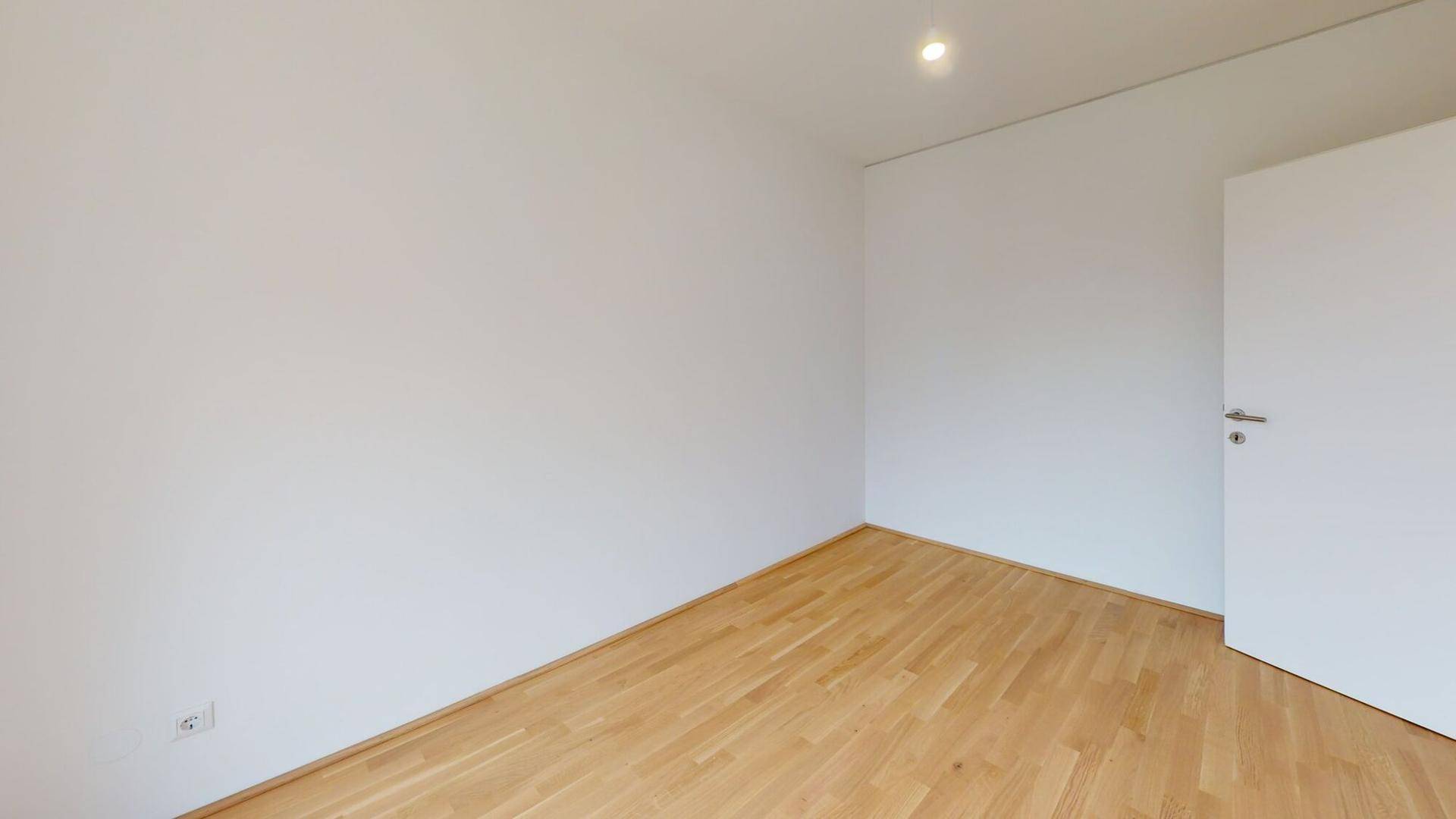 Helles Schlafzimmer mit Holzboden und weißen Wänden, bereit zur individuellen Gestaltung.