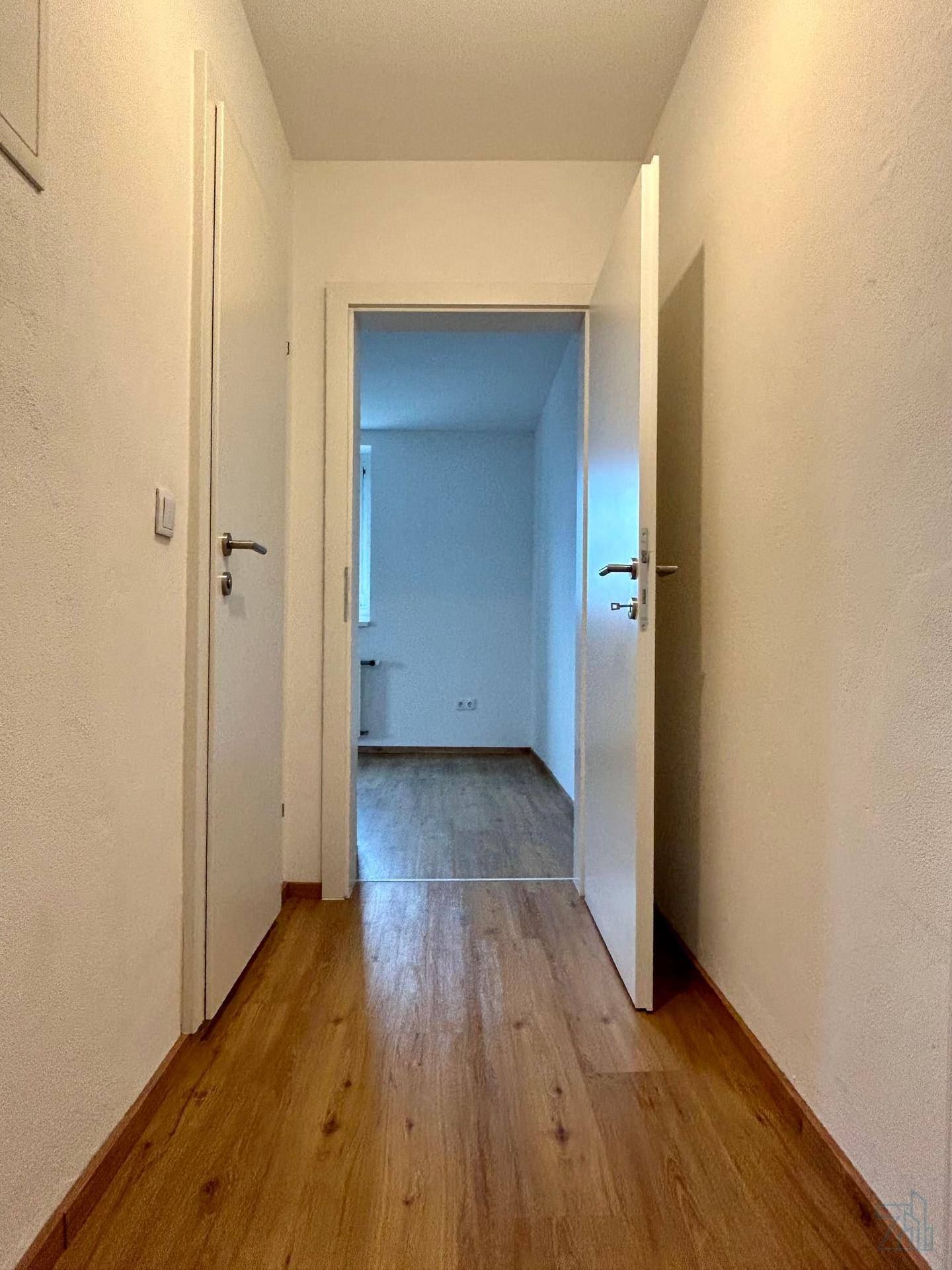 Schmaler Flur mit Laminatboden und weißen Türen, der zu weiteren Räumen führt.