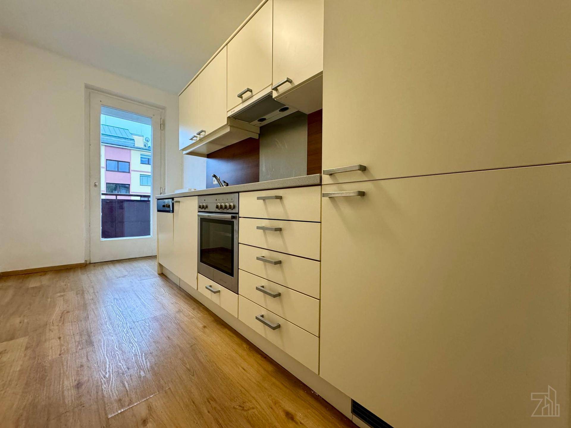 Helle Küche mit beigen Schränken, integrierten Geräten und Zugang zum Balkon.