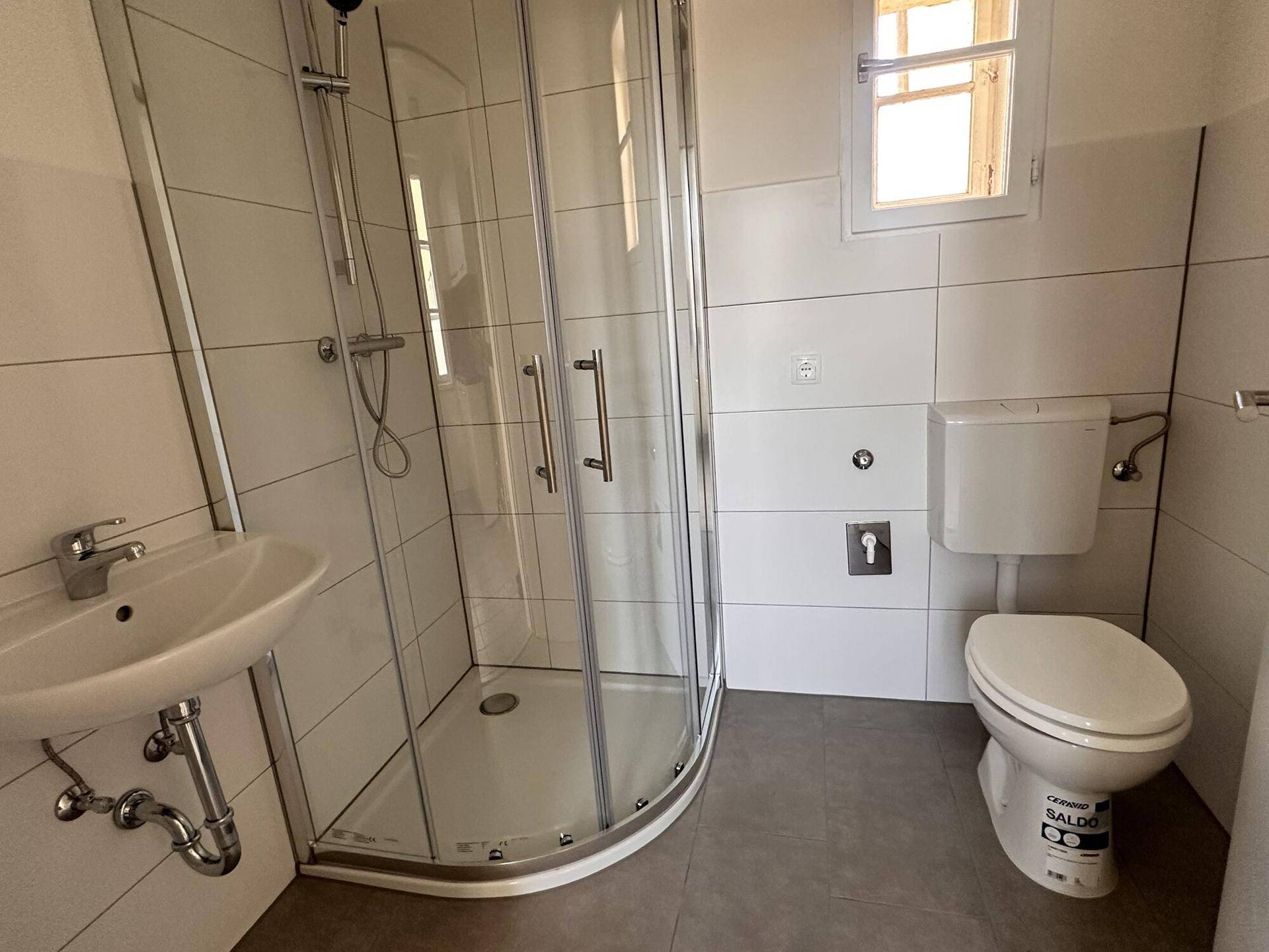 Modernes Badezimmer mit Duschkabine, WC, Waschbecken und weißen Fliesen.