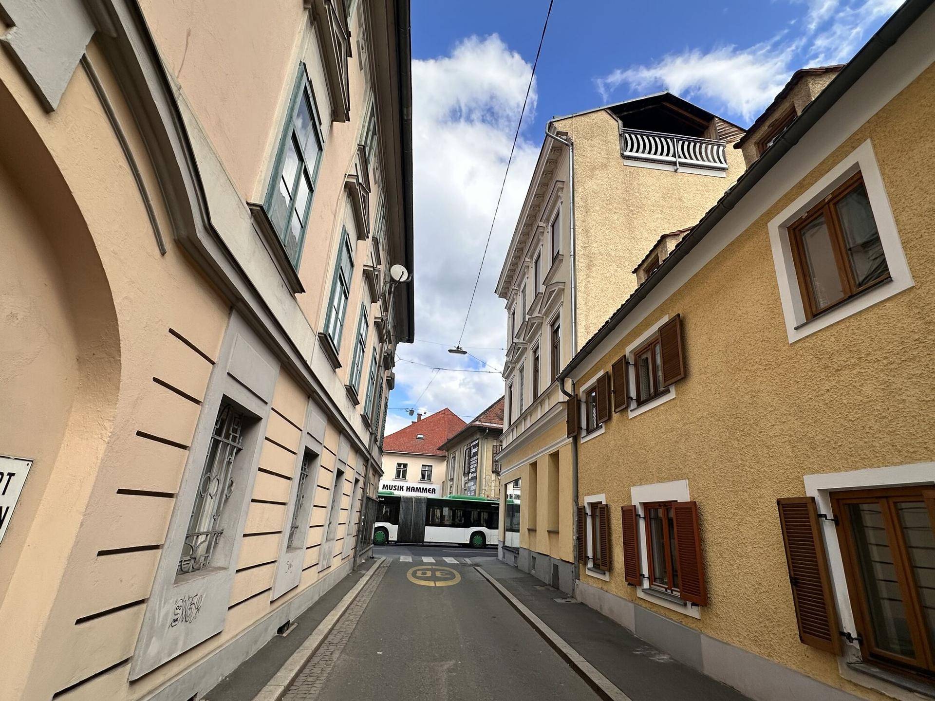 Enge Gasse in der Stadt mit historischen Gebäuden und einem Bus im Hintergrund.