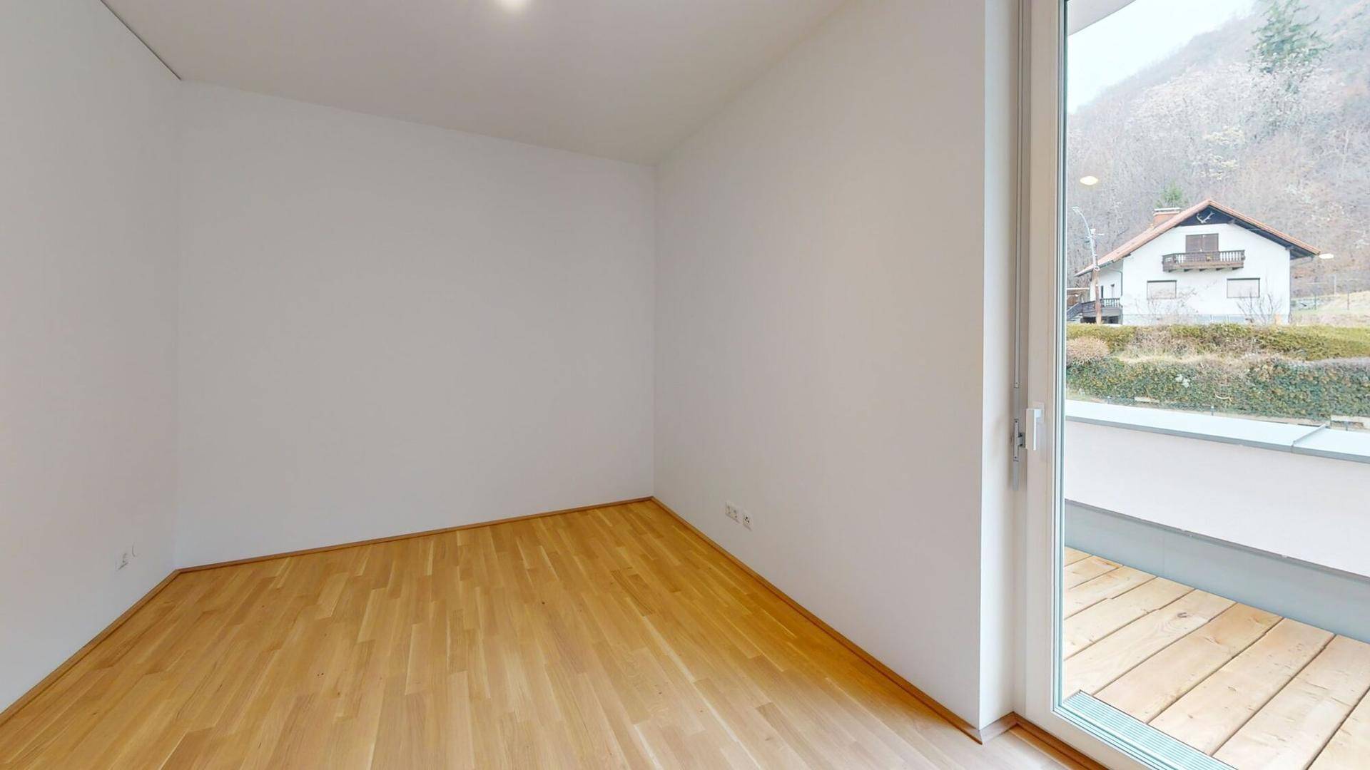 Helles Zimmer mit Holzboden und Terrassenzugang, bietet einen Blick auf ein gegenüberliegendes Haus.